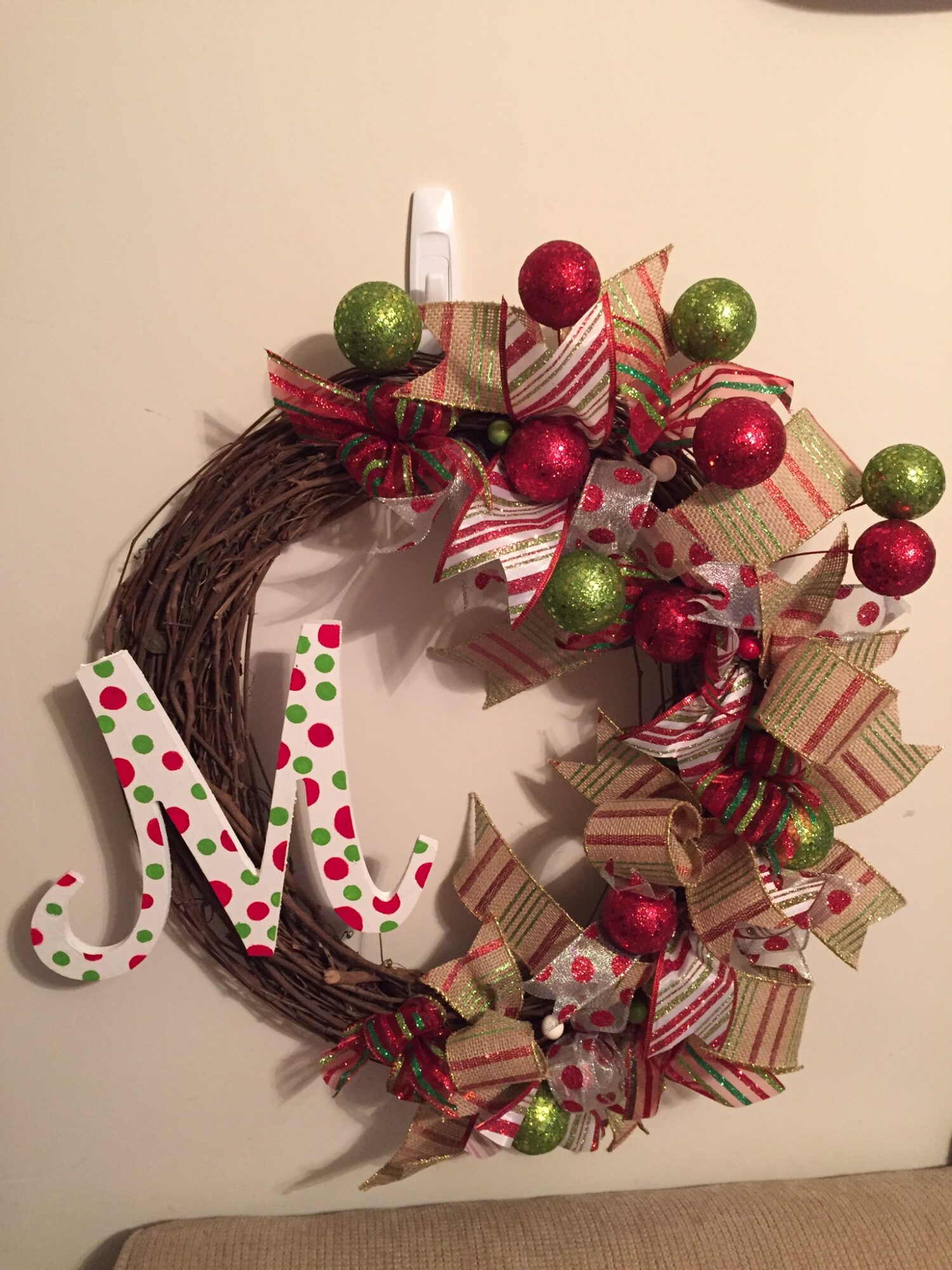 Christmas wreath decorated with red and green ornaments, ribbon bows, and a white and green polka dot letter J.