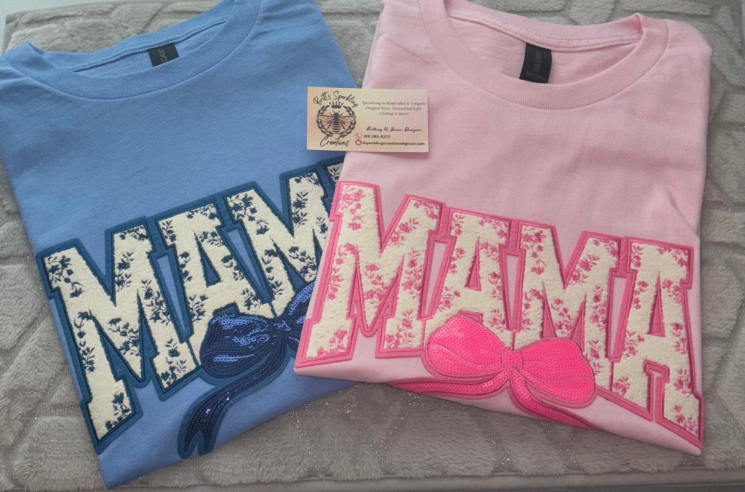Two folded T-shirts, one blue and one pink, with large text and bow designs, placed on a gray surface.