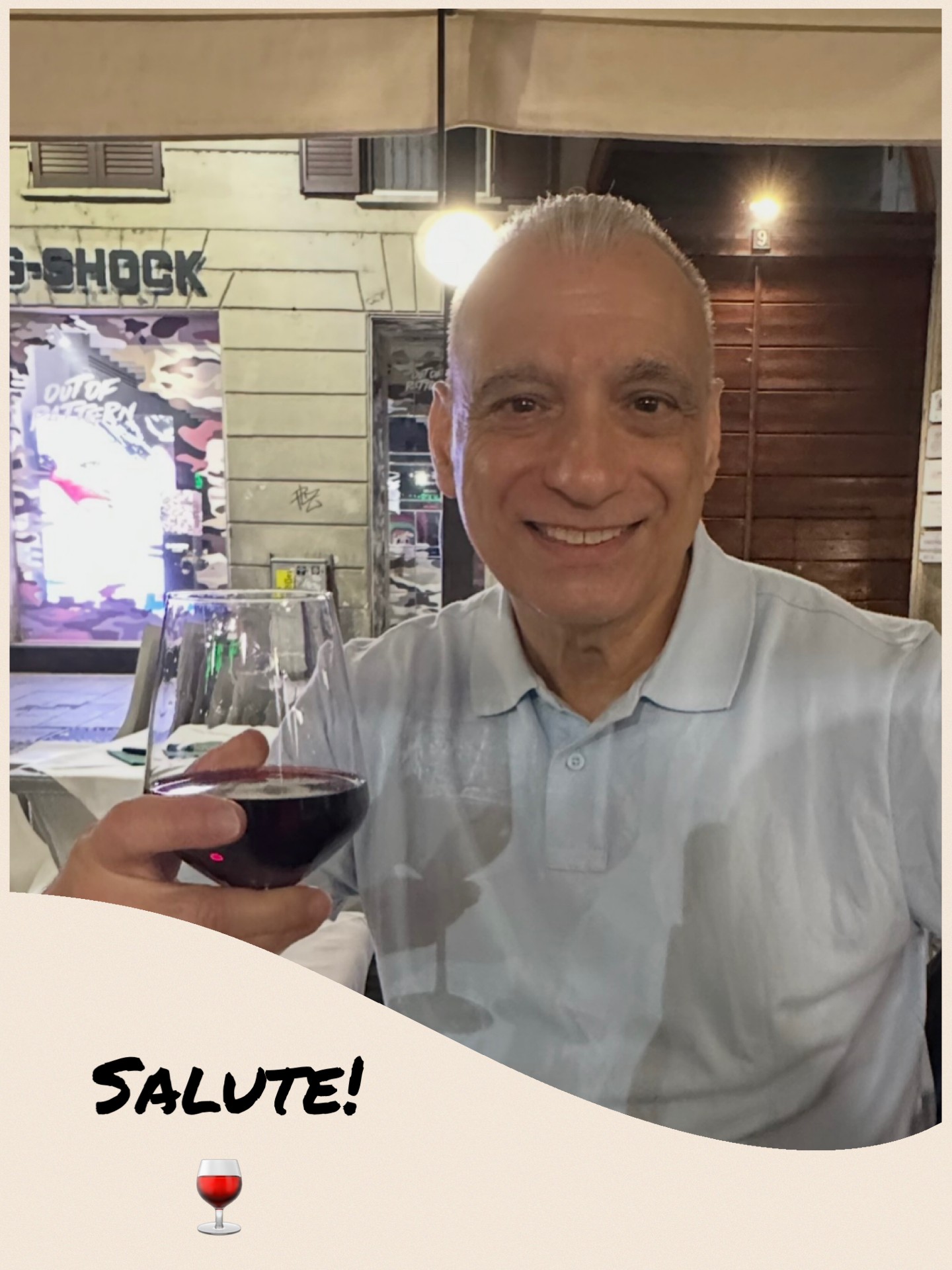 Smiling man in a white shirt holding a glass of red wine in a restaurant setting.