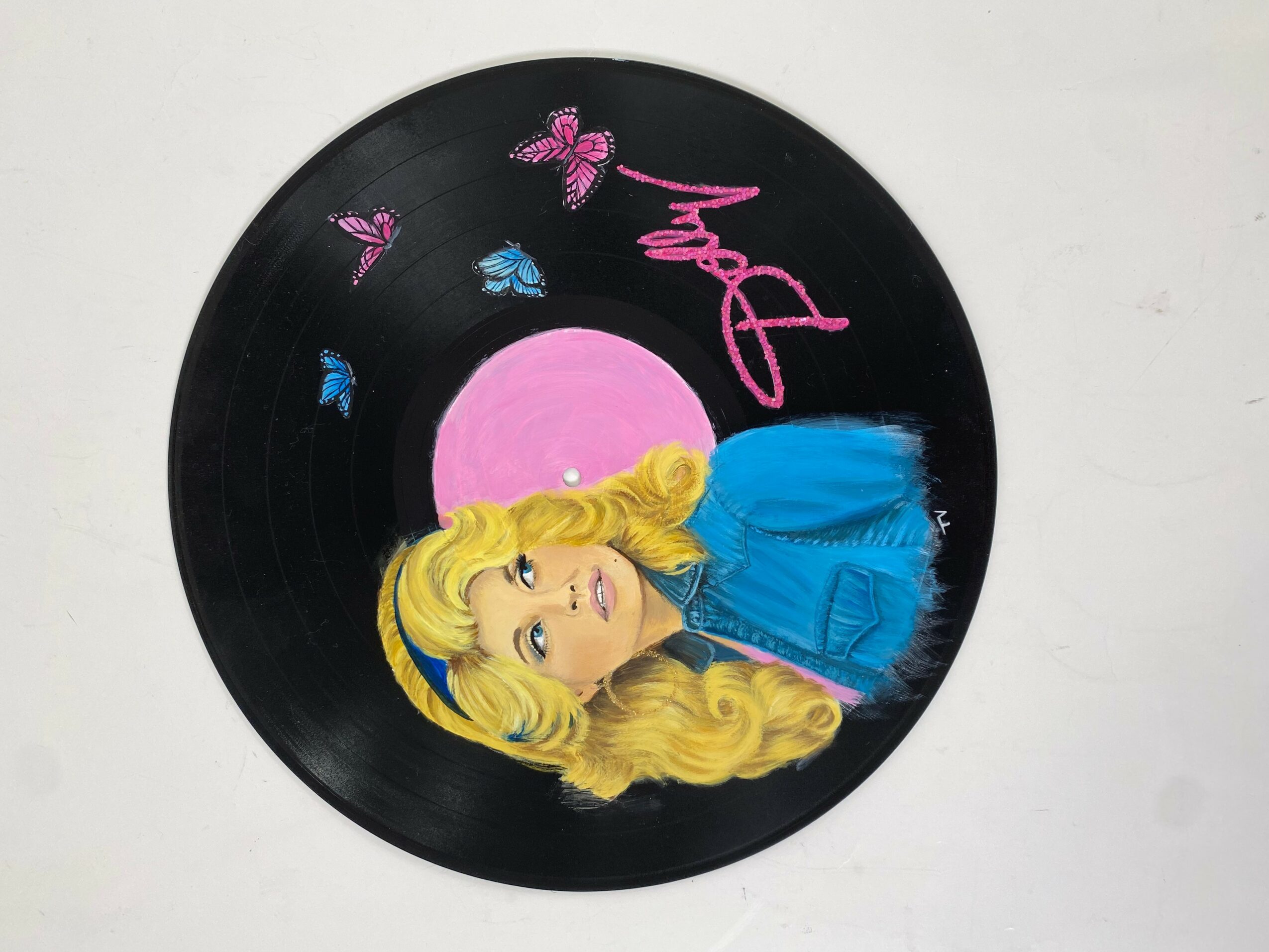 Vinyl record with a colorful illustration of a woman with long blonde hair, blue dress, pink moon, and butterflies, and the word 'Music'.