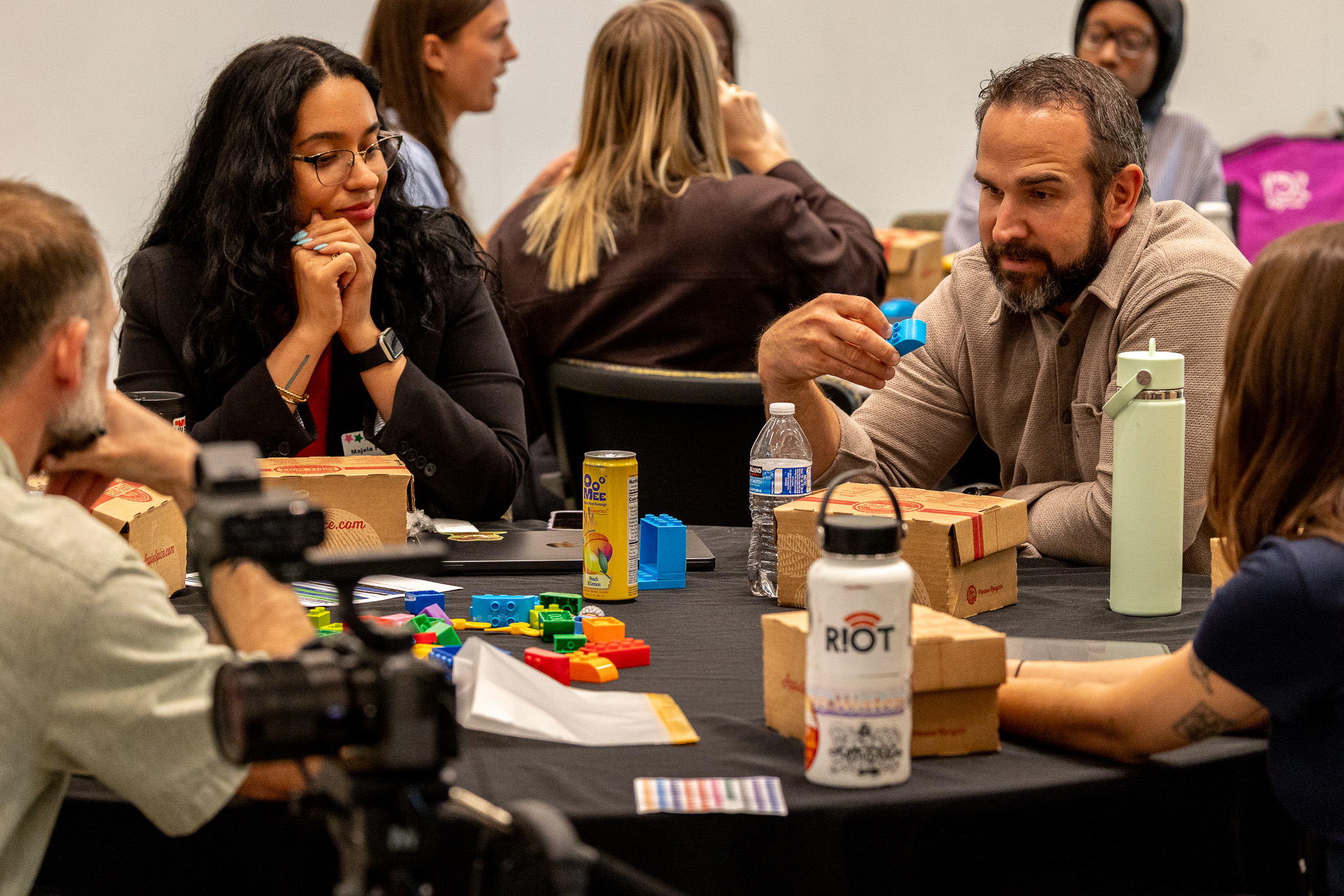 Group of people playing a board game at a table, with various game pieces and drinks, in a social setting.