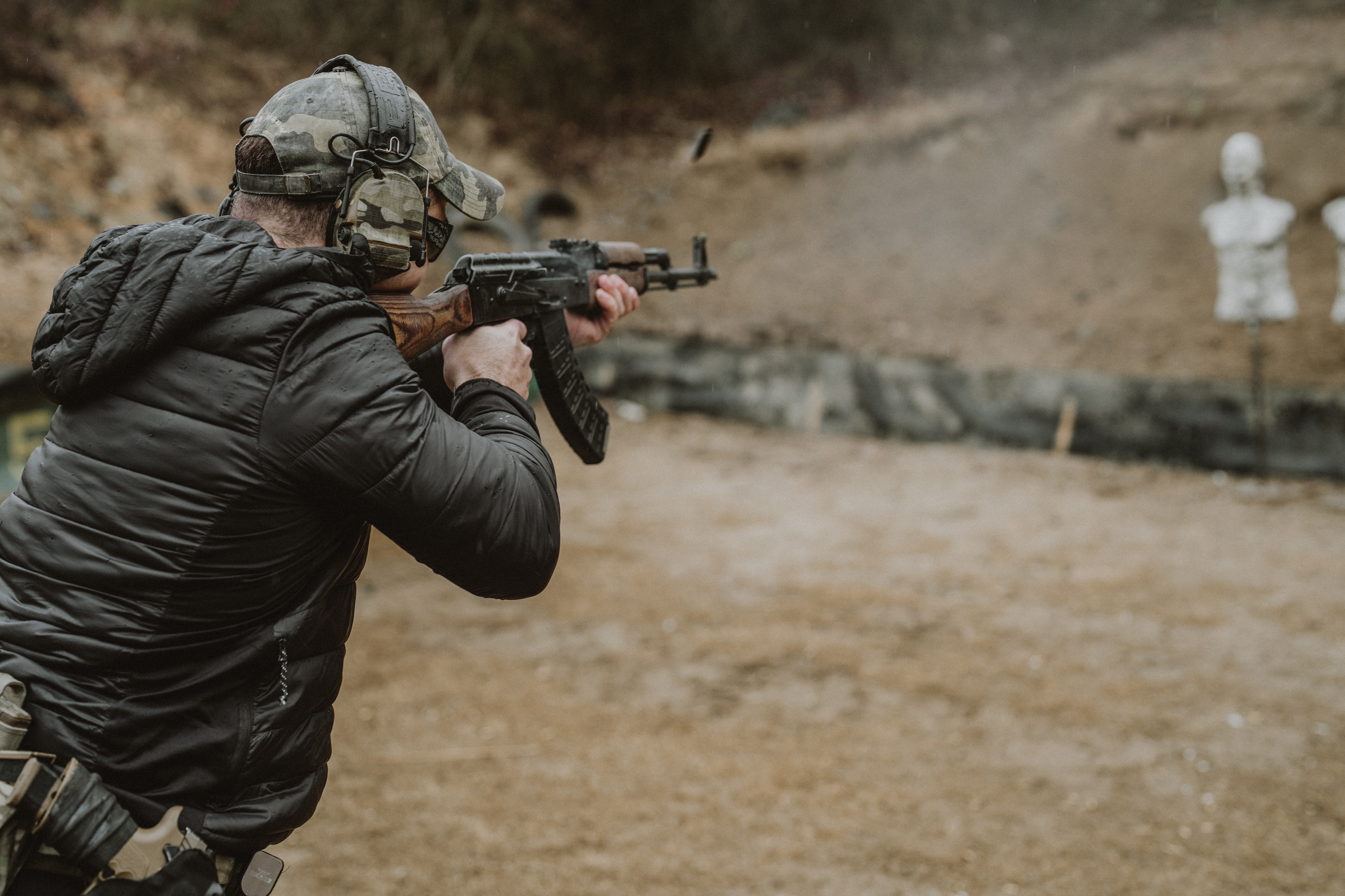 Person in tactical gear aiming a rifle at targets outdoors, with two white targets in the background.