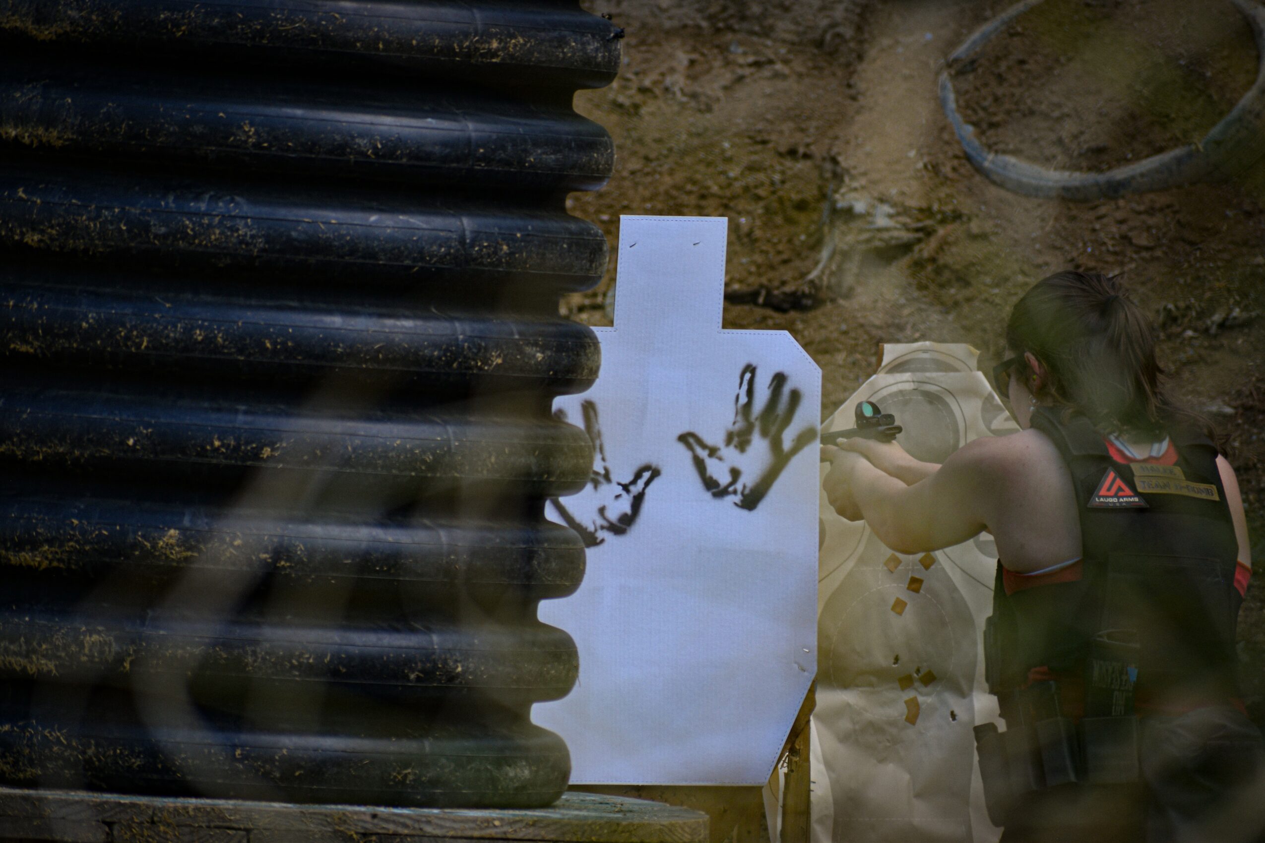 Person working outdoors with a backpack, digging or examining the ground, with a black corrugated pipe nearby and a white paper with a handprint.