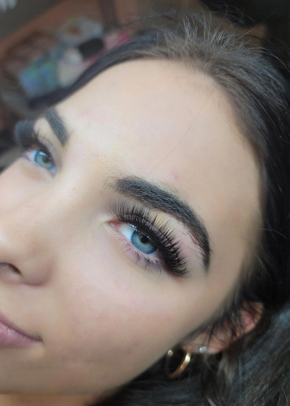 Close-up of a woman's face showing blue eyes, long eyelashes, and dark eyebrows.