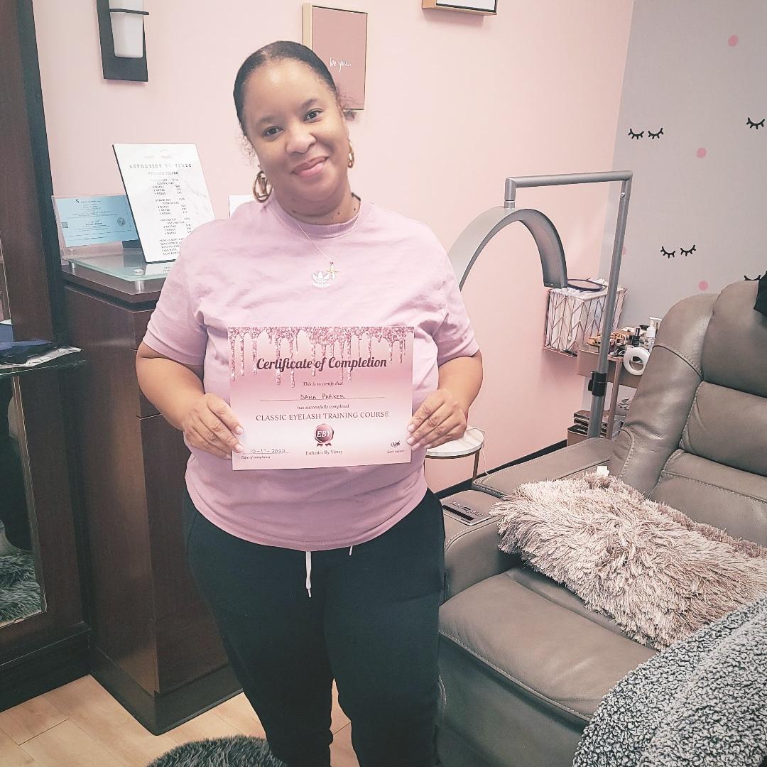 Woman holding a certificate, standing in a room with pink walls and furniture, smiling at the camera.