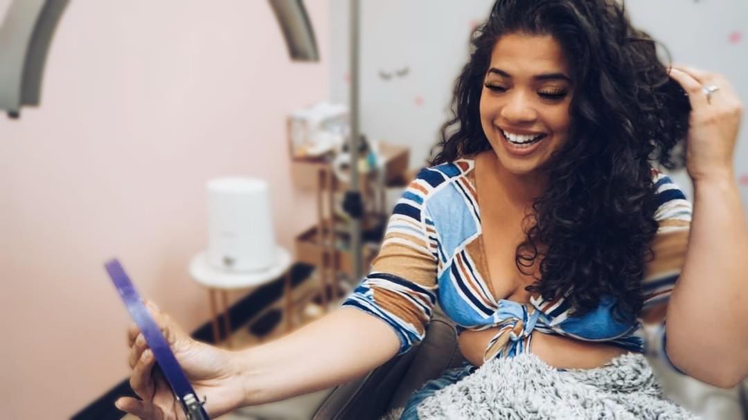 Young woman with curly hair smiling and looking at a tablet in a room with medical equipment.