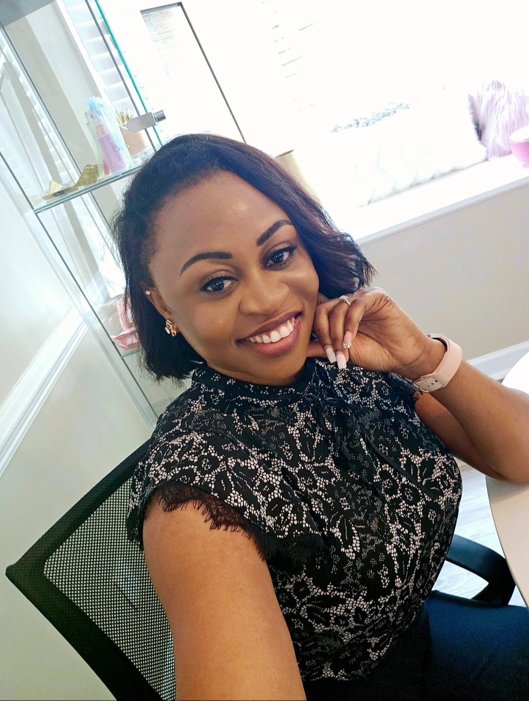 Smiling woman with short dark hair, wearing a black lace top, sitting in a modern office, looking at the camera.