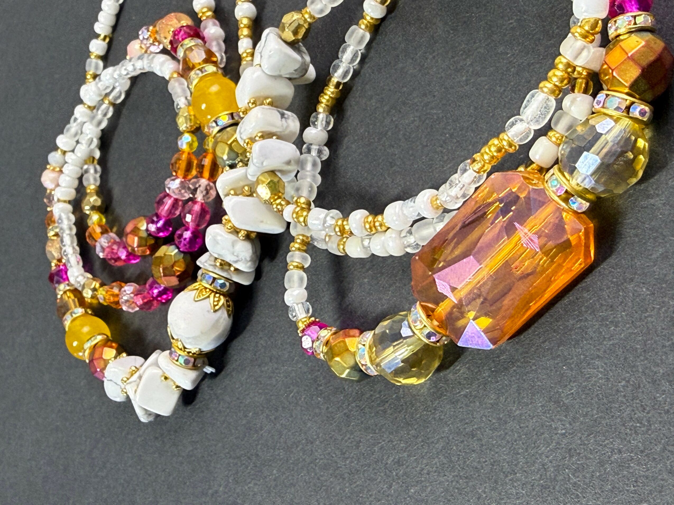 Multiple colorful beaded necklaces with white, yellow, pink, and orange beads on a dark background.
