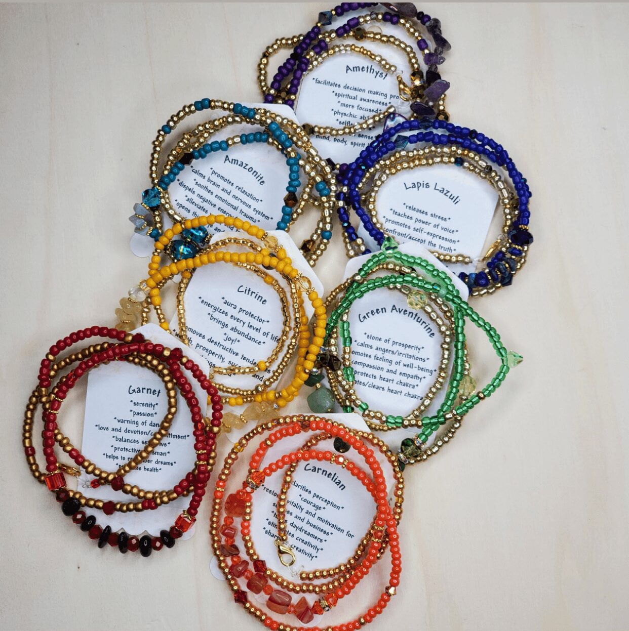 Multiple colorful beaded necklaces arranged in a circle on a light surface, each with a paper label inside.