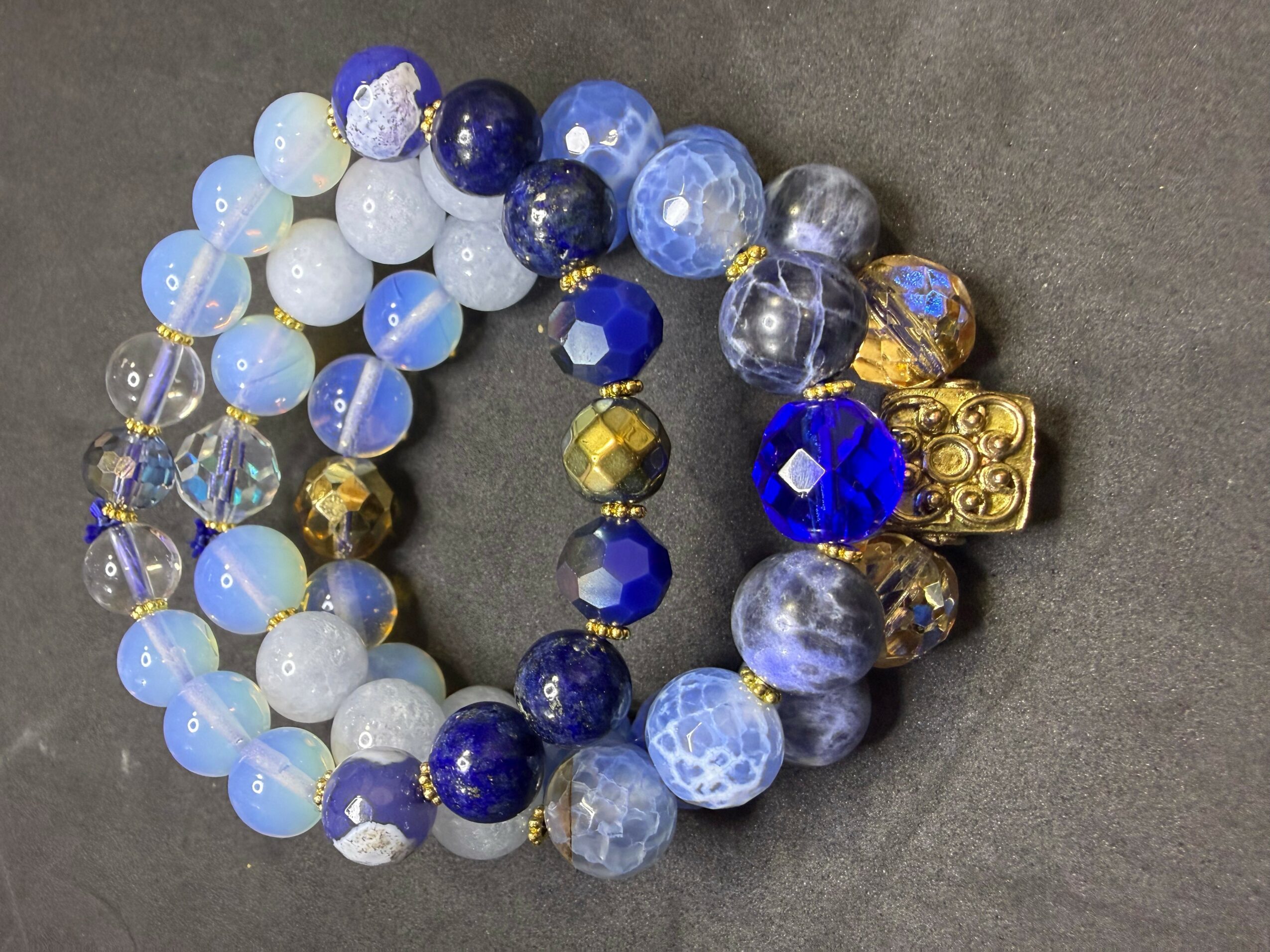 Three beaded bracelets with blue, white, and gold beads, arranged on a dark surface.