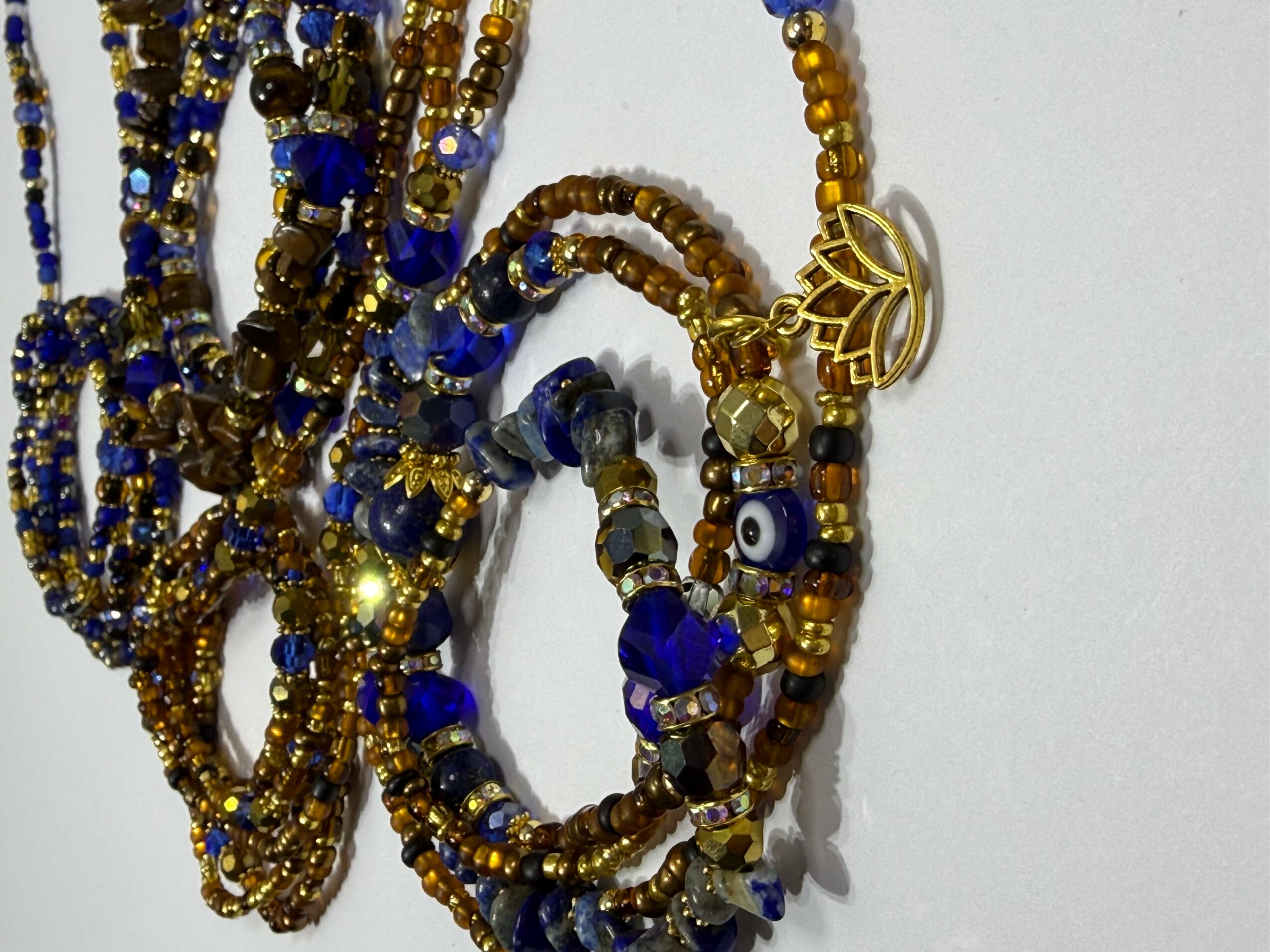 Multiple beaded necklaces with gold, blue, and eye-shaped beads, arranged on a white background.
