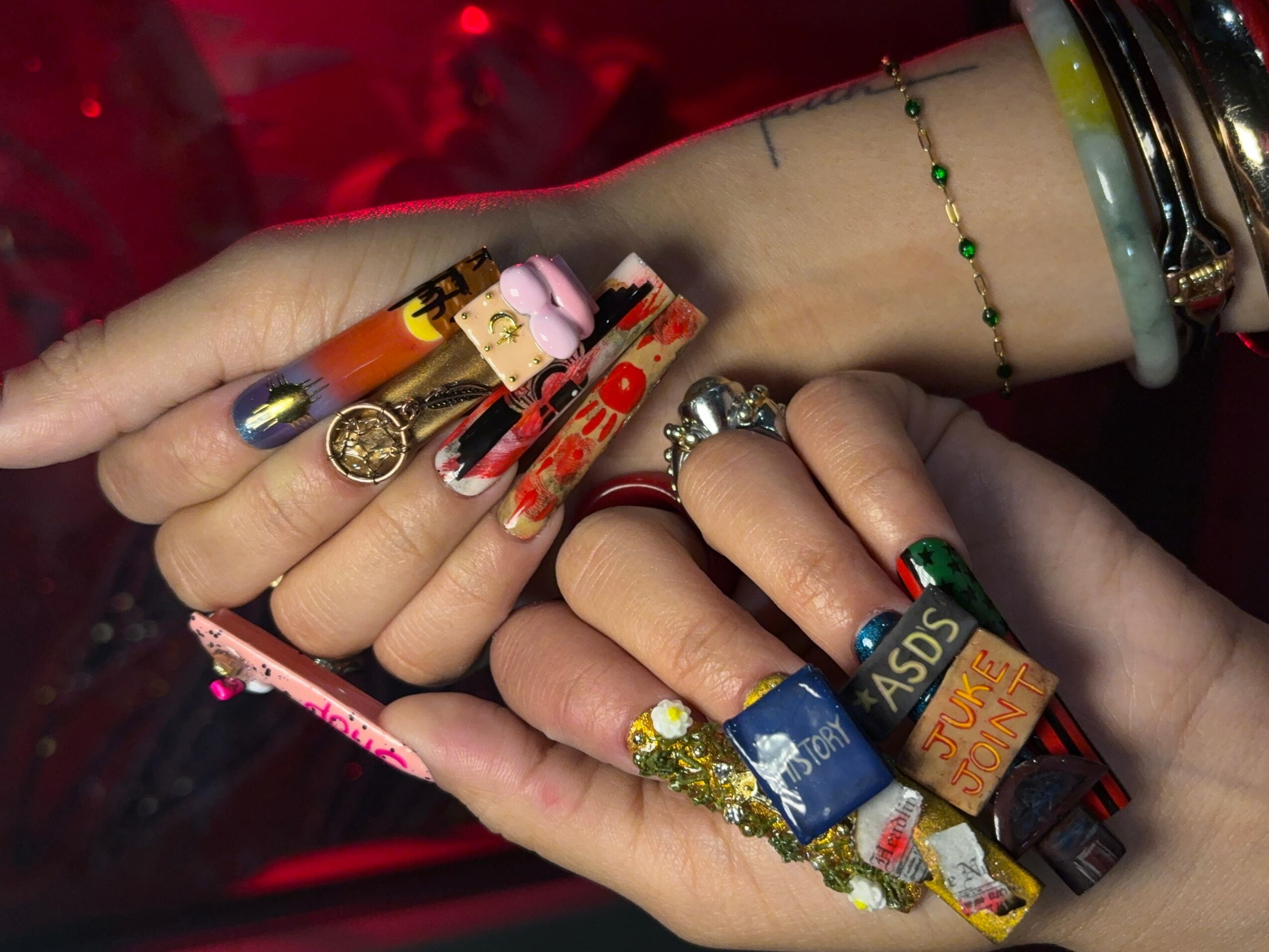 Two hands with decorated nails and multiple rings, bracelets, and accessories, intertwined against a red background.