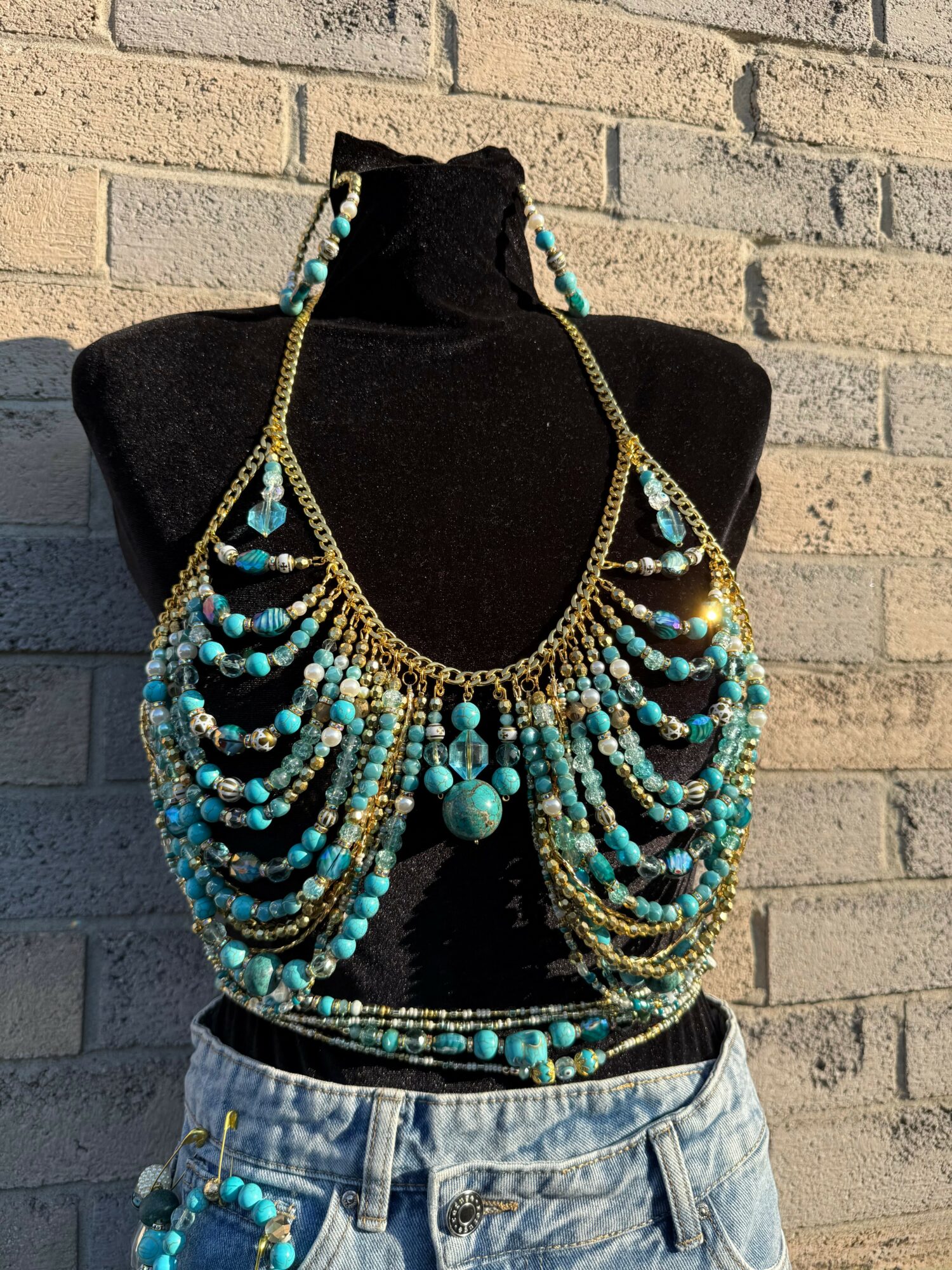 Necklace with multiple strands of turquoise and gold beads displayed on a black mannequin bust against a brick wall.