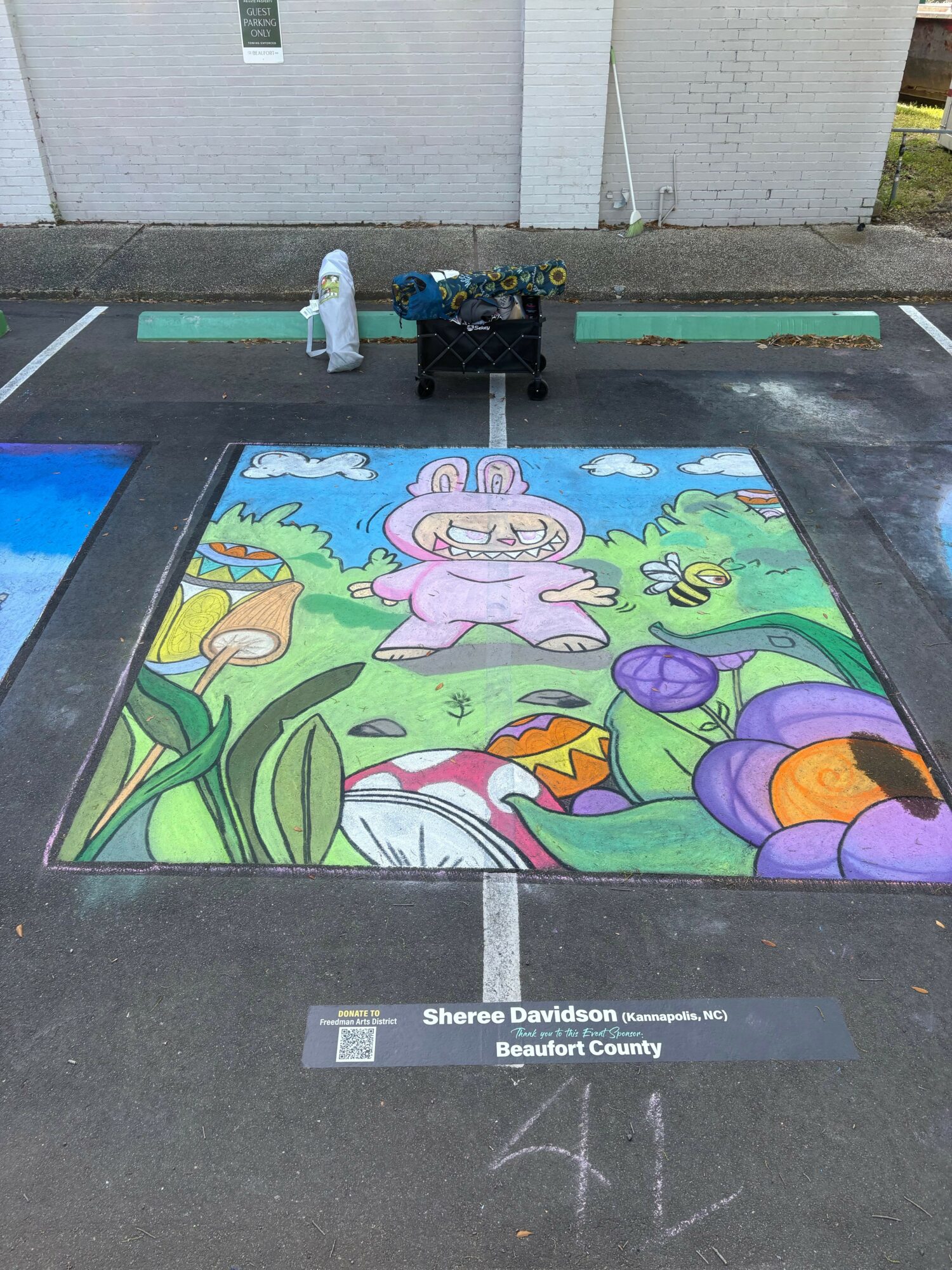 Children drawing colorful chalk art on a sidewalk with buildings in the background.
