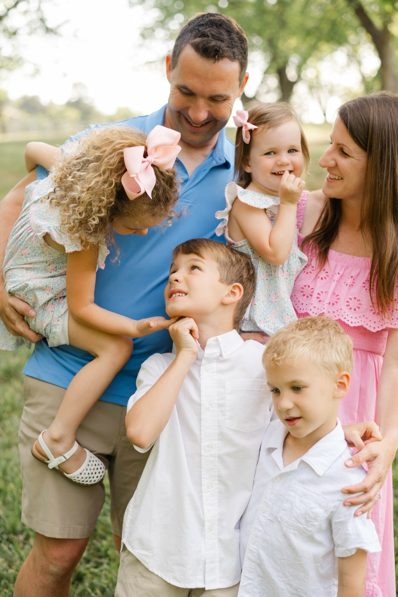 Family of five outdoors, smiling and interacting, with trees in the background.