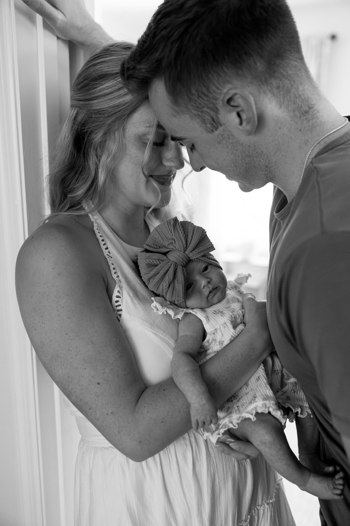 A woman holding a newborn baby, with a man leaning in close, all smiling and touching foreheads.
