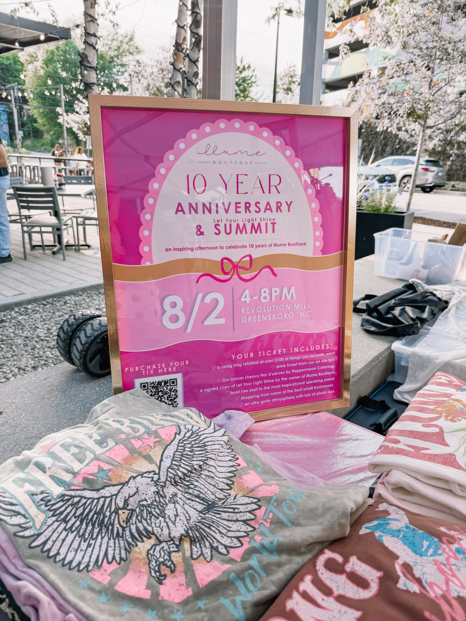 Pink and white poster advertising a 10-year anniversary and summit event, with date, time, and QR code, placed outdoors.