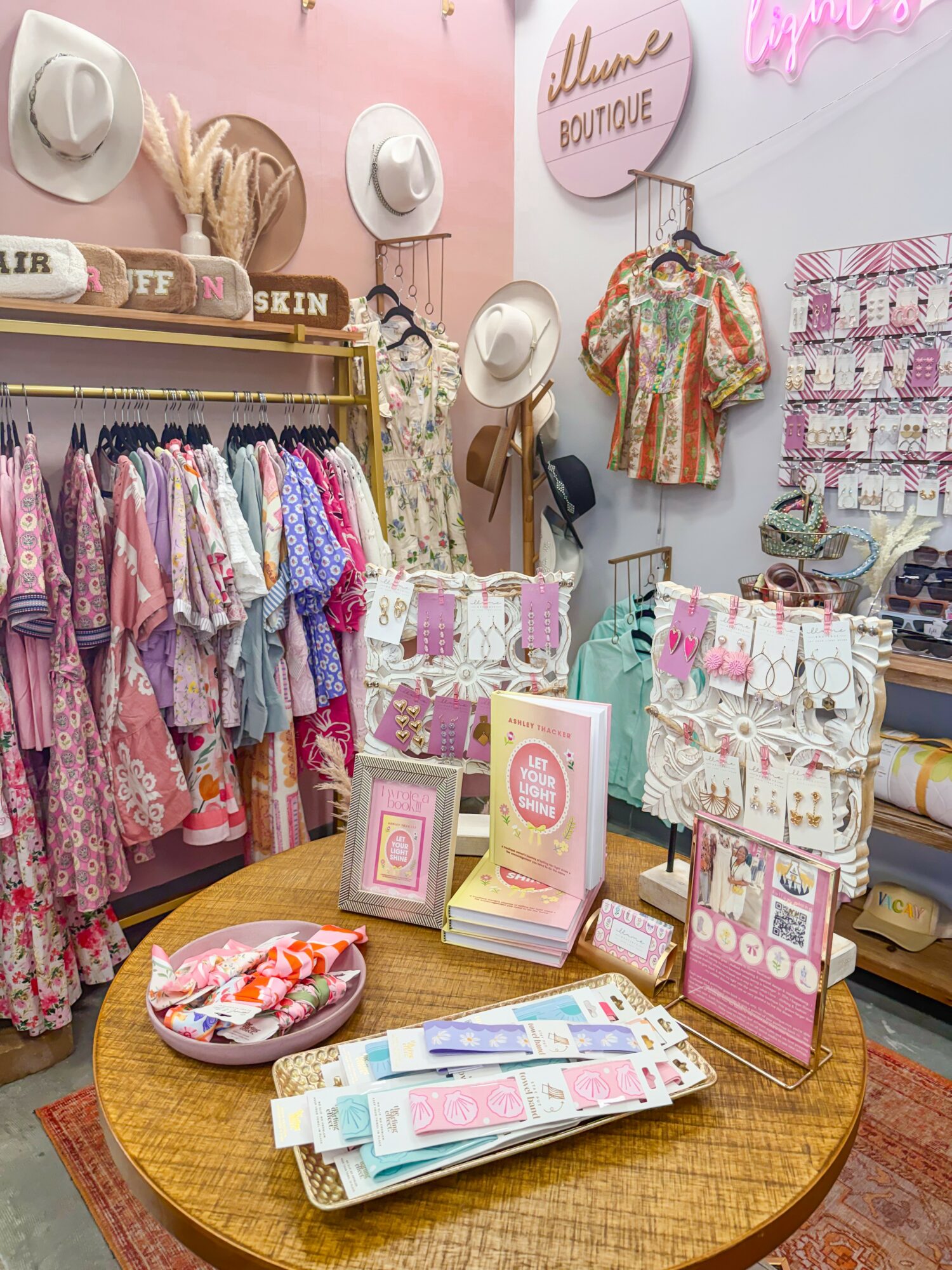 Display of hats, clothing, and accessories in a boutique with pink walls and decorative signs.