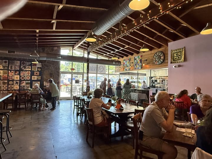 Interior of a lively cafe with people sitting at tables, large windows, and decorative wall art.