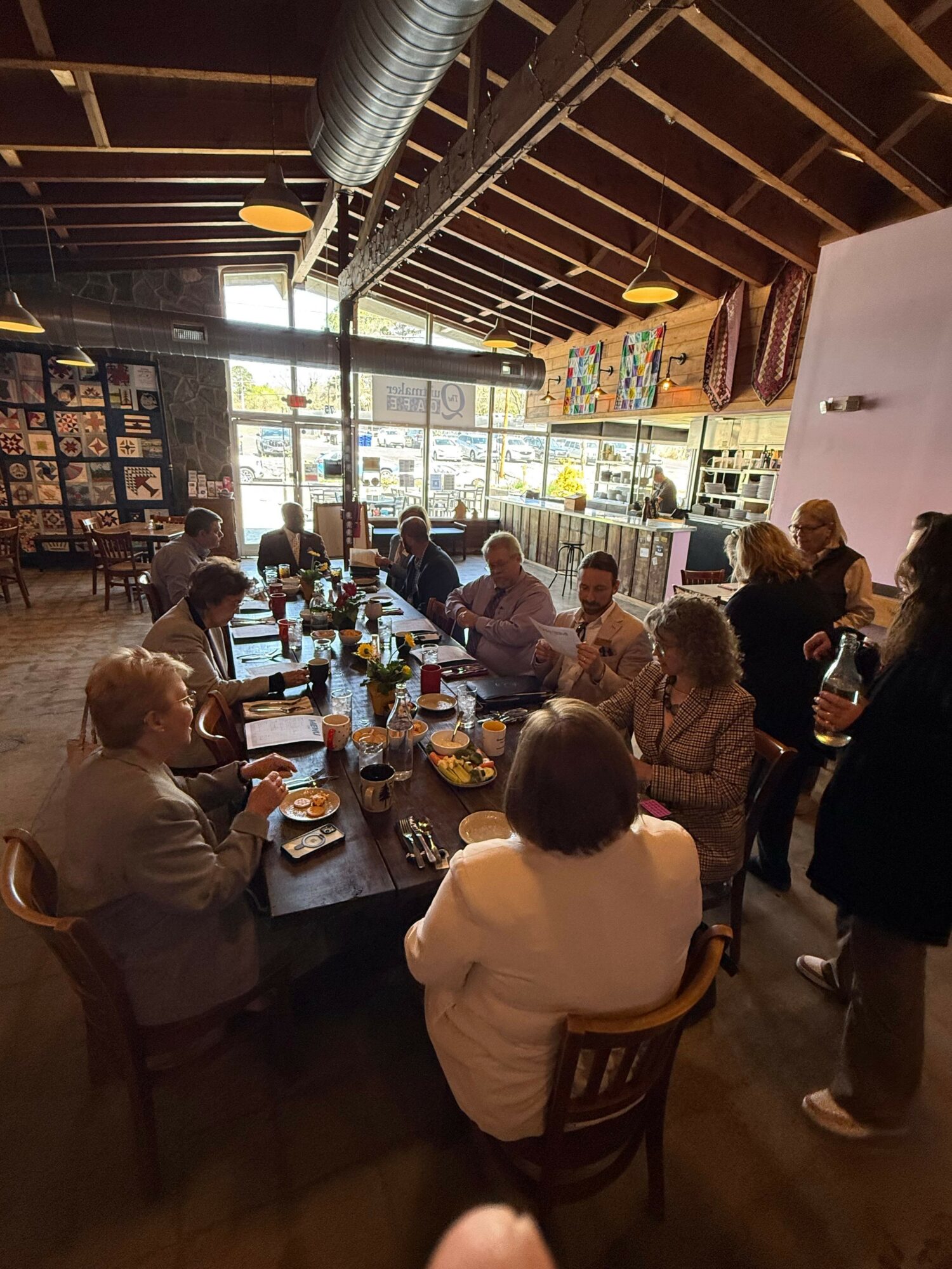 People gathered around a table in a restaurant, with a large window and artwork on the wall behind them.