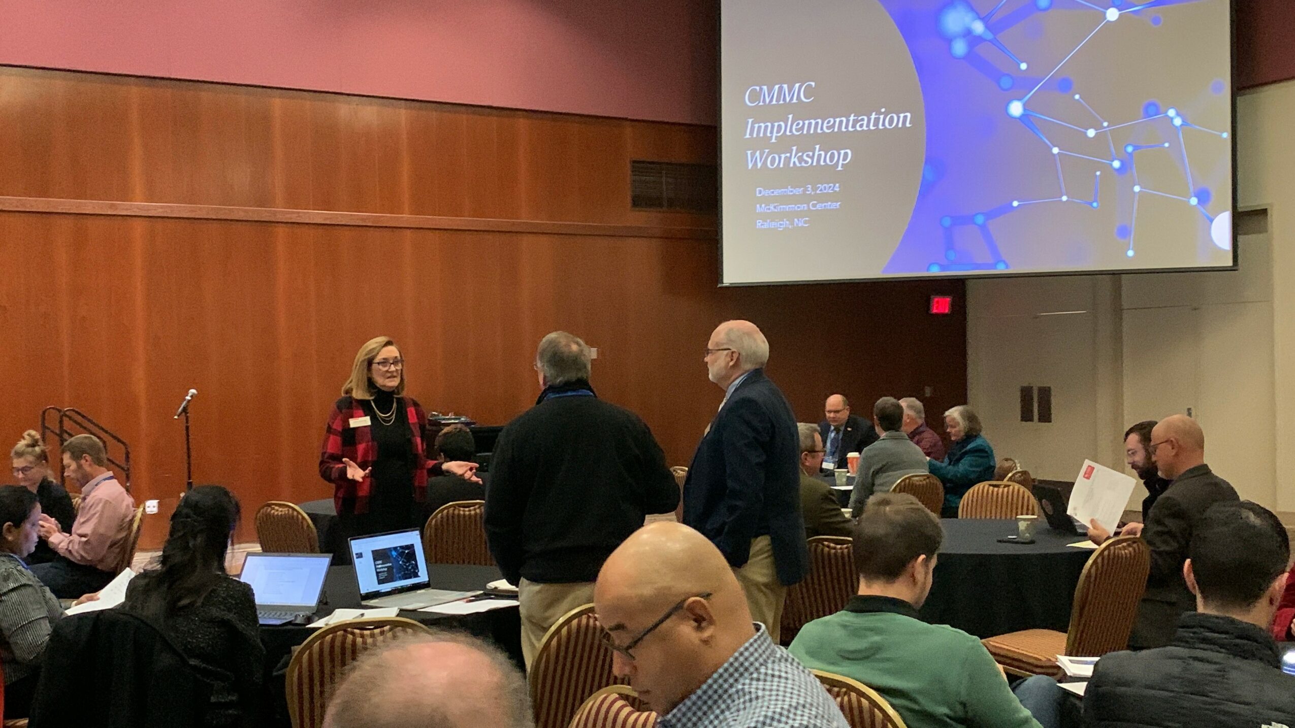 People attending a workshop in a conference room with a presentation screen displaying a slide titled 'GAMC Application Implementation Workshop.'