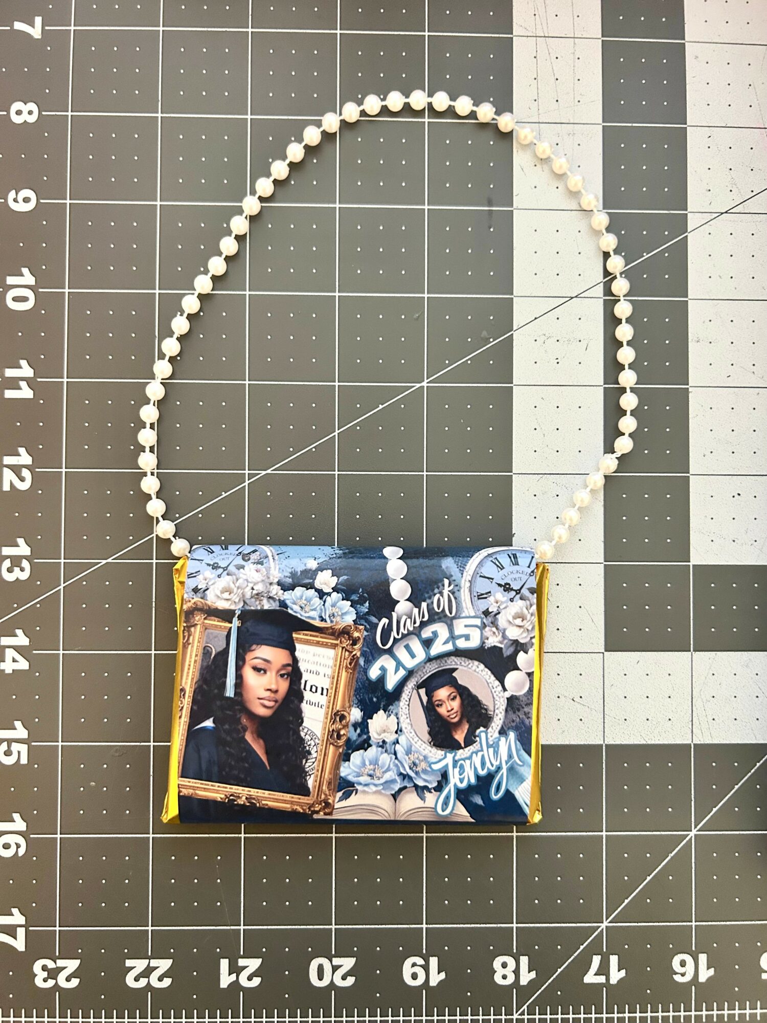 Necklace with a pendant featuring a photo of a young woman, decorated with blue and white floral designs, on a cutting mat.