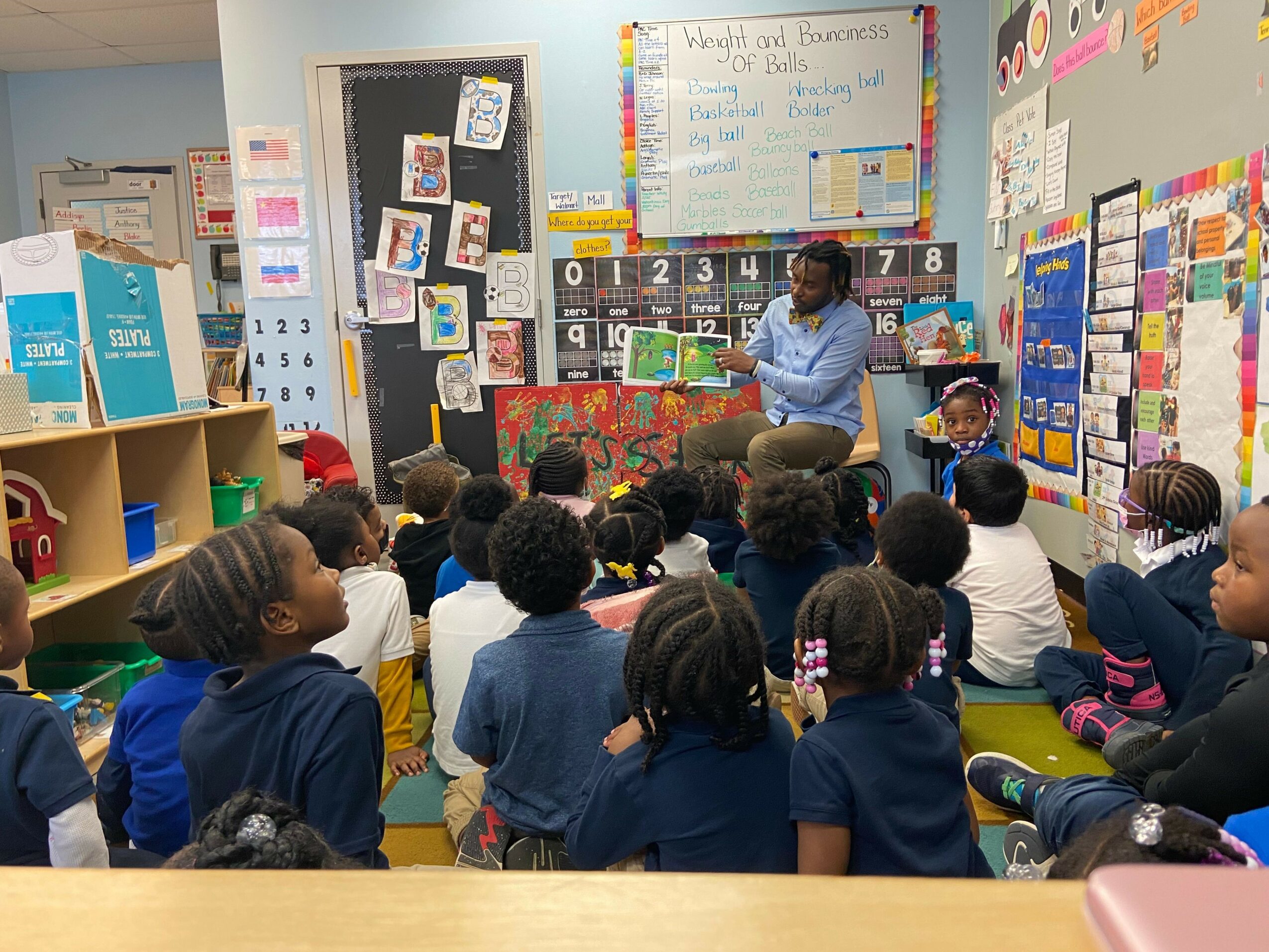 Children sit at a table in a classroom, engaging in a learning activity with colorful materials and posters on the wall.