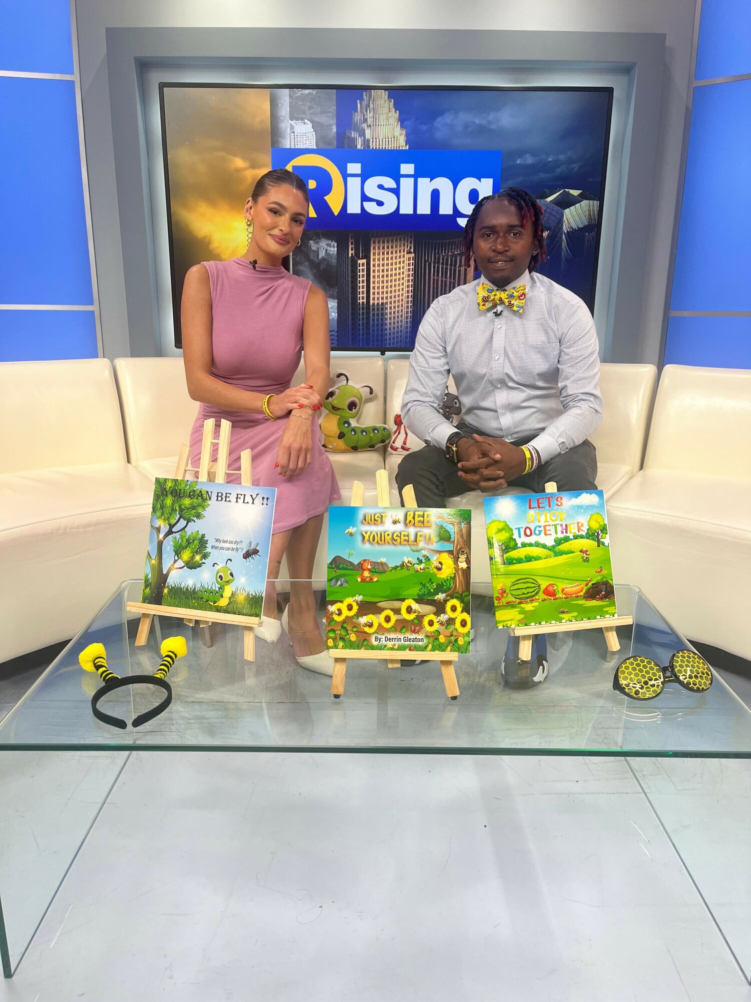Two people standing behind a table with gardening supplies and plants, indoors with a blue wall and a screen in the background.