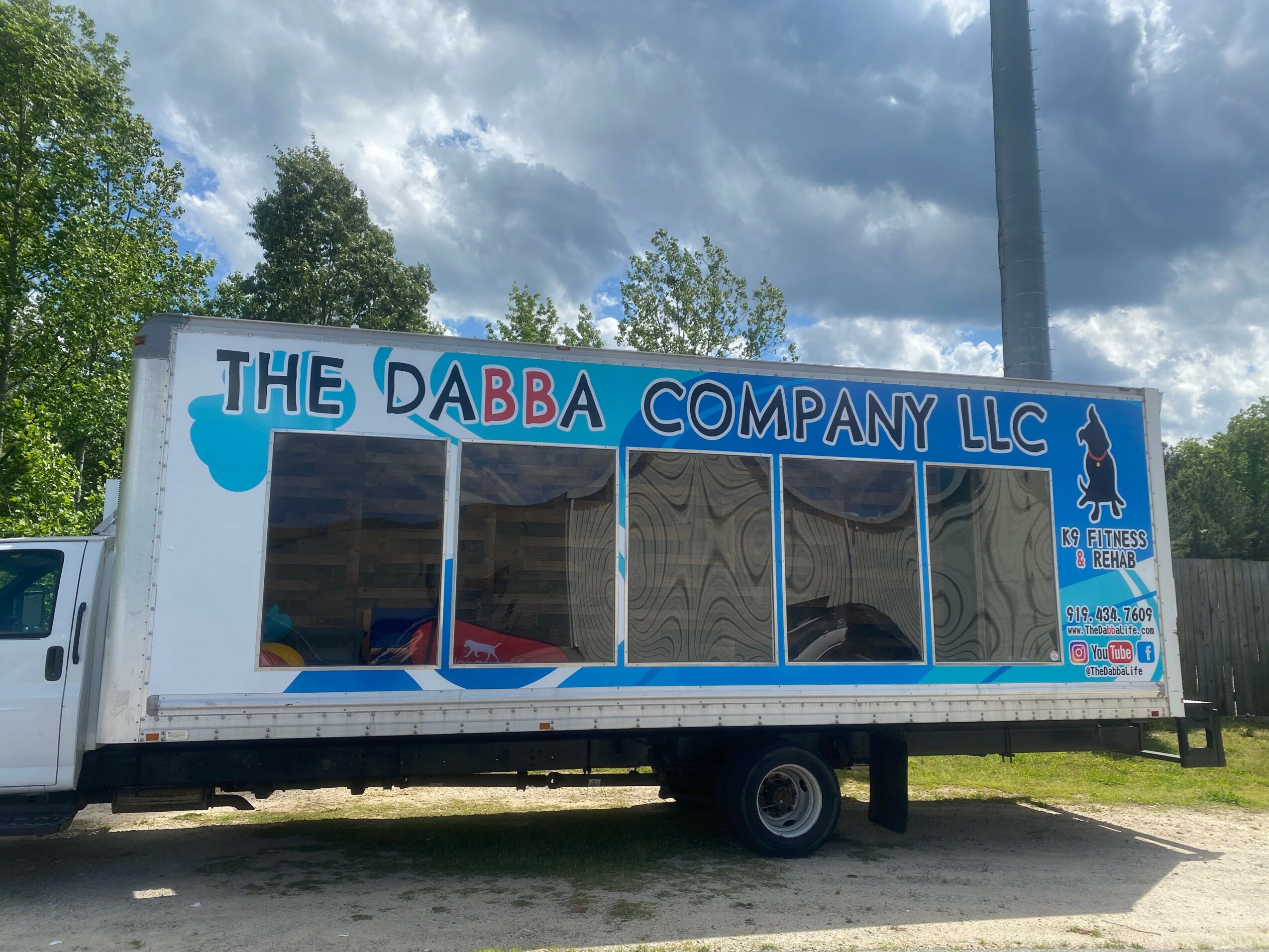 Side view of a mobile business truck with the sign 'The Dabba Company LLC' and a penguin logo, parked outdoors.