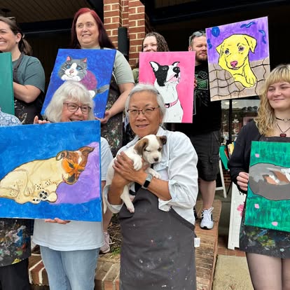 Group of people holding colorful animal paintings outdoors, with a woman holding a puppy in the center.