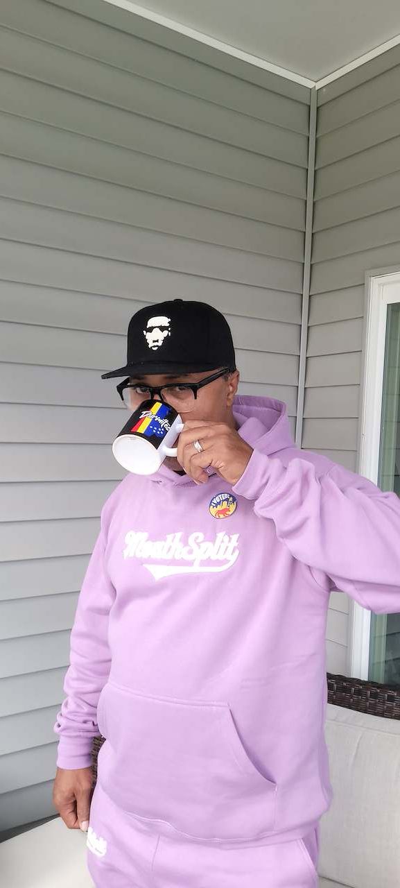 Person in a pink hoodie holding a cup and a bottle, standing outside near a house with siding.
