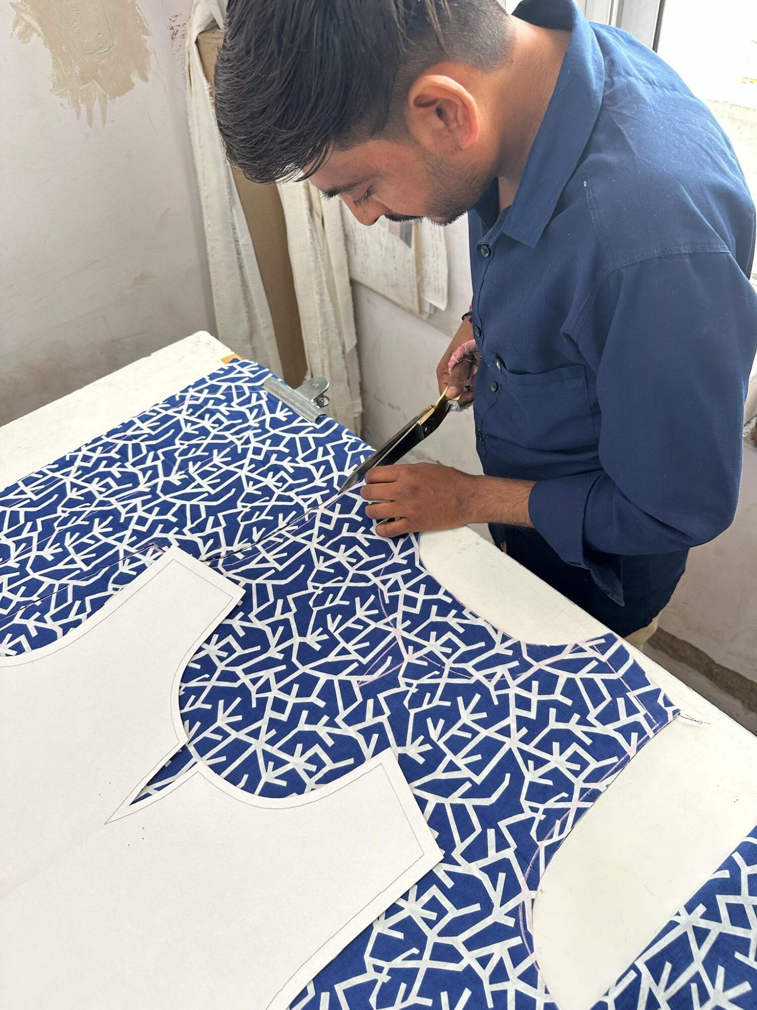 Person working on a large fabric with a blue and white mosaic pattern, cutting with a tool, in a room with a window.
