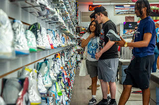 Three people shopping in a sneaker store aisle, looking at shoes on shelves, with a Nike sign in the background.