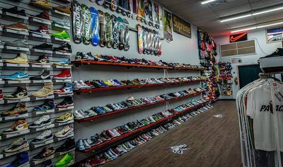 Shoe store with shelves filled with various shoes, backpacks hanging on the wall, and a wooden floor.