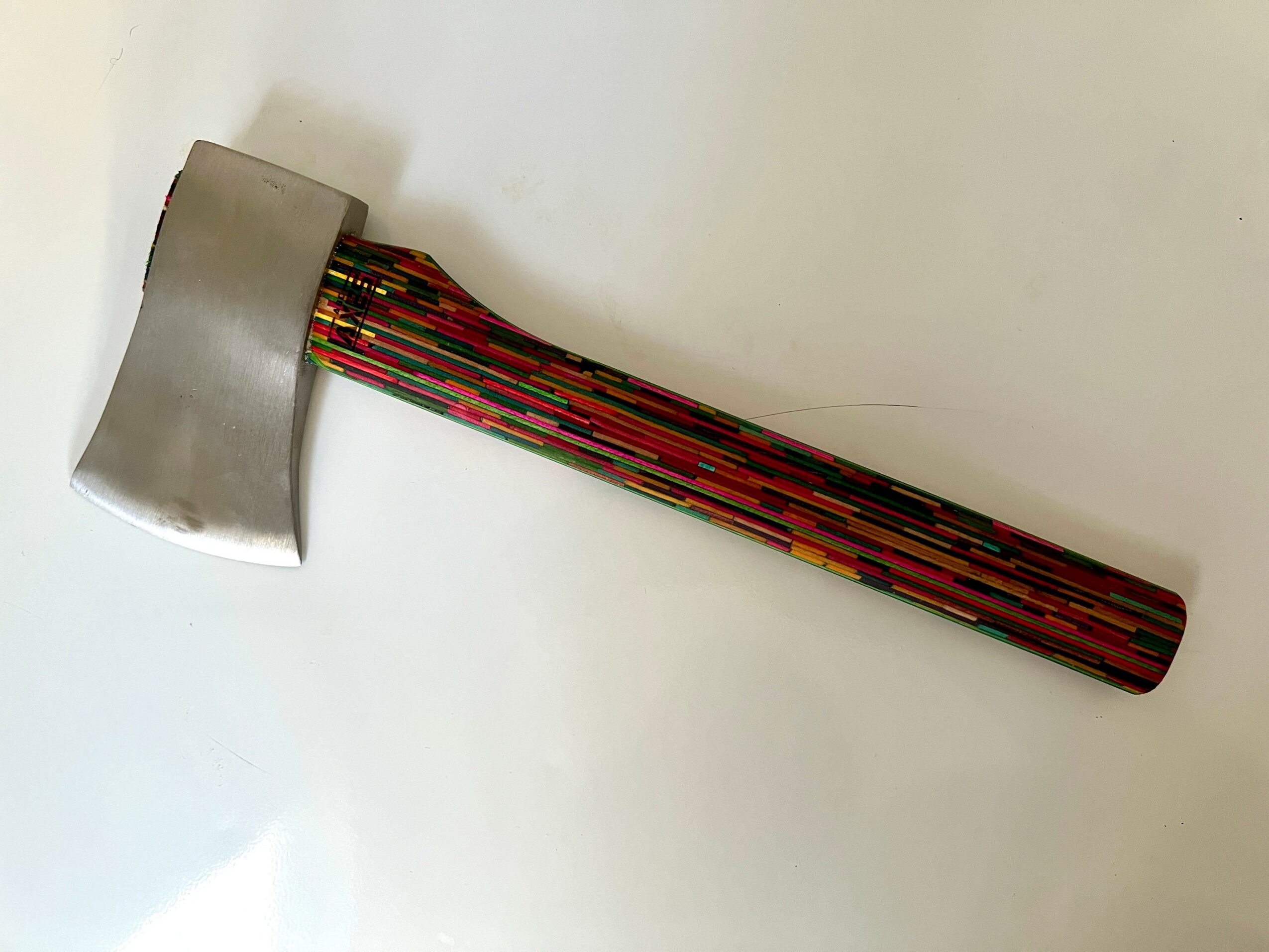 A metal axe head attached to a colorful, striped handle, lying on a white surface.