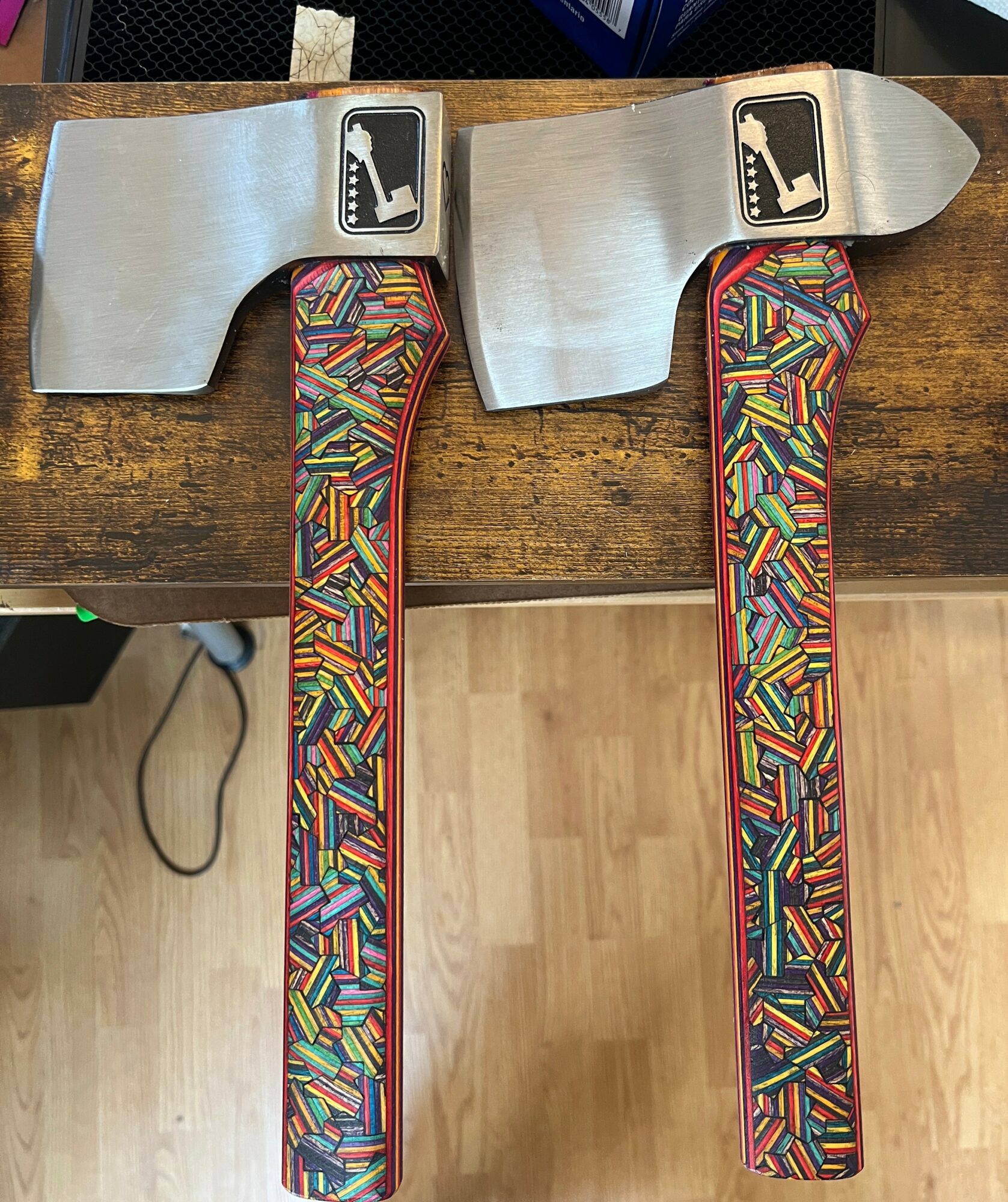 Two metal objects with colorful, patterned handles on a wooden surface, with a light-colored floor below.
