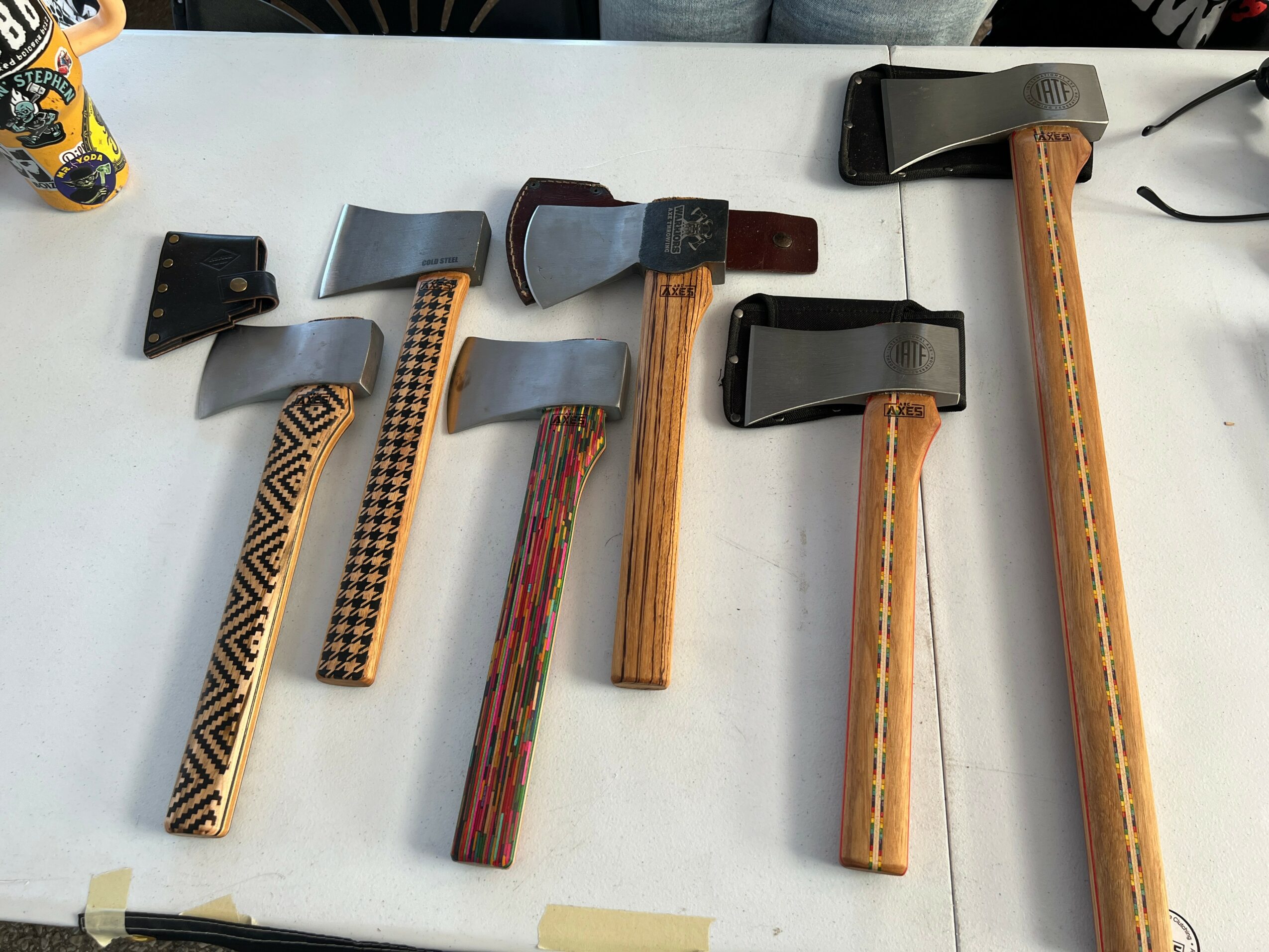 Five axes with different handles and blade designs are laid out on a white surface.