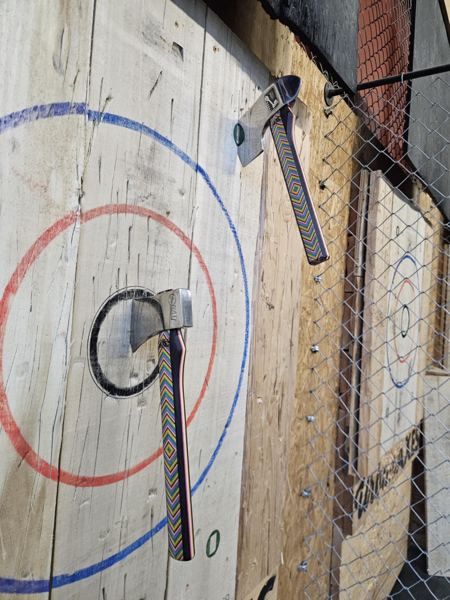 Two metal rings with colorful straps are mounted on a wooden wall with painted target circles, next to a chain-link fence.