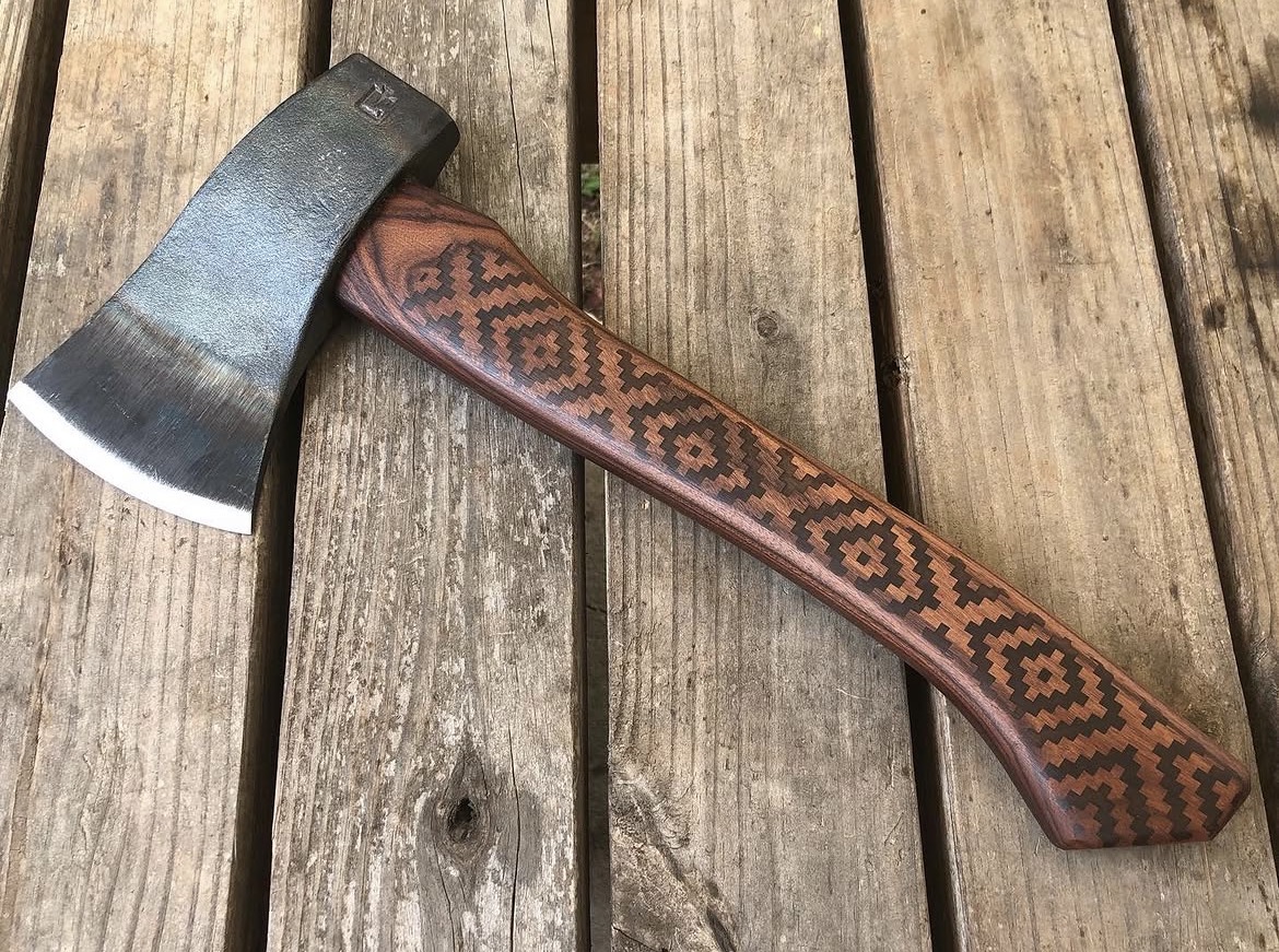 A hatchet with a patterned wooden handle resting on a wooden surface.