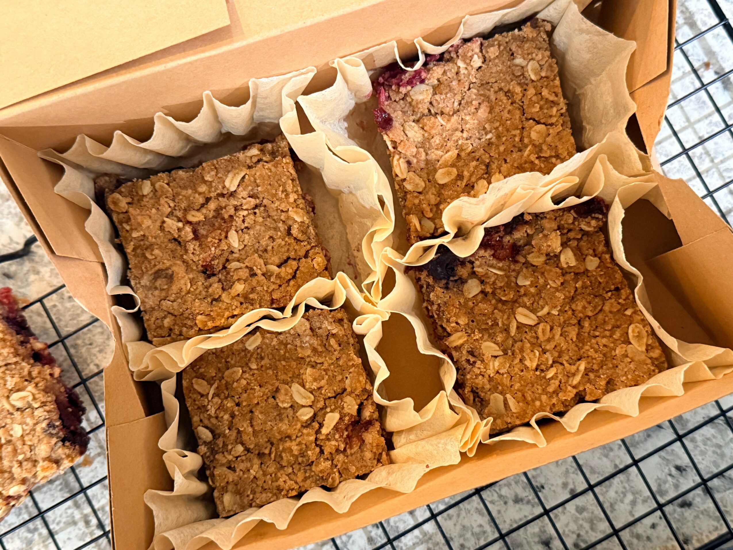 Four square crumbly baked bars in a box with parchment paper, viewed from above.