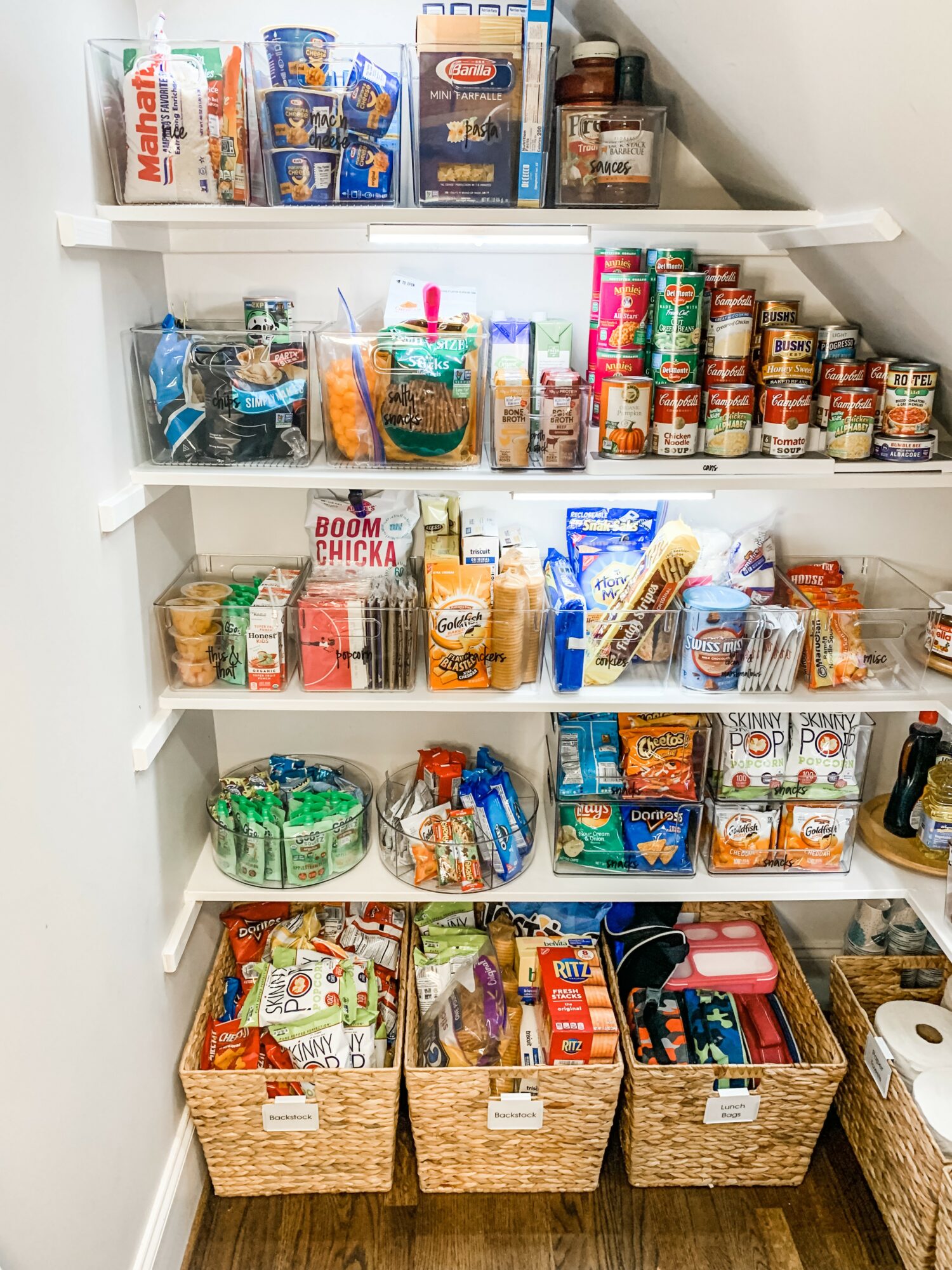 Open pantry with snacks, canned goods, and baskets of food items on shelves and in baskets.