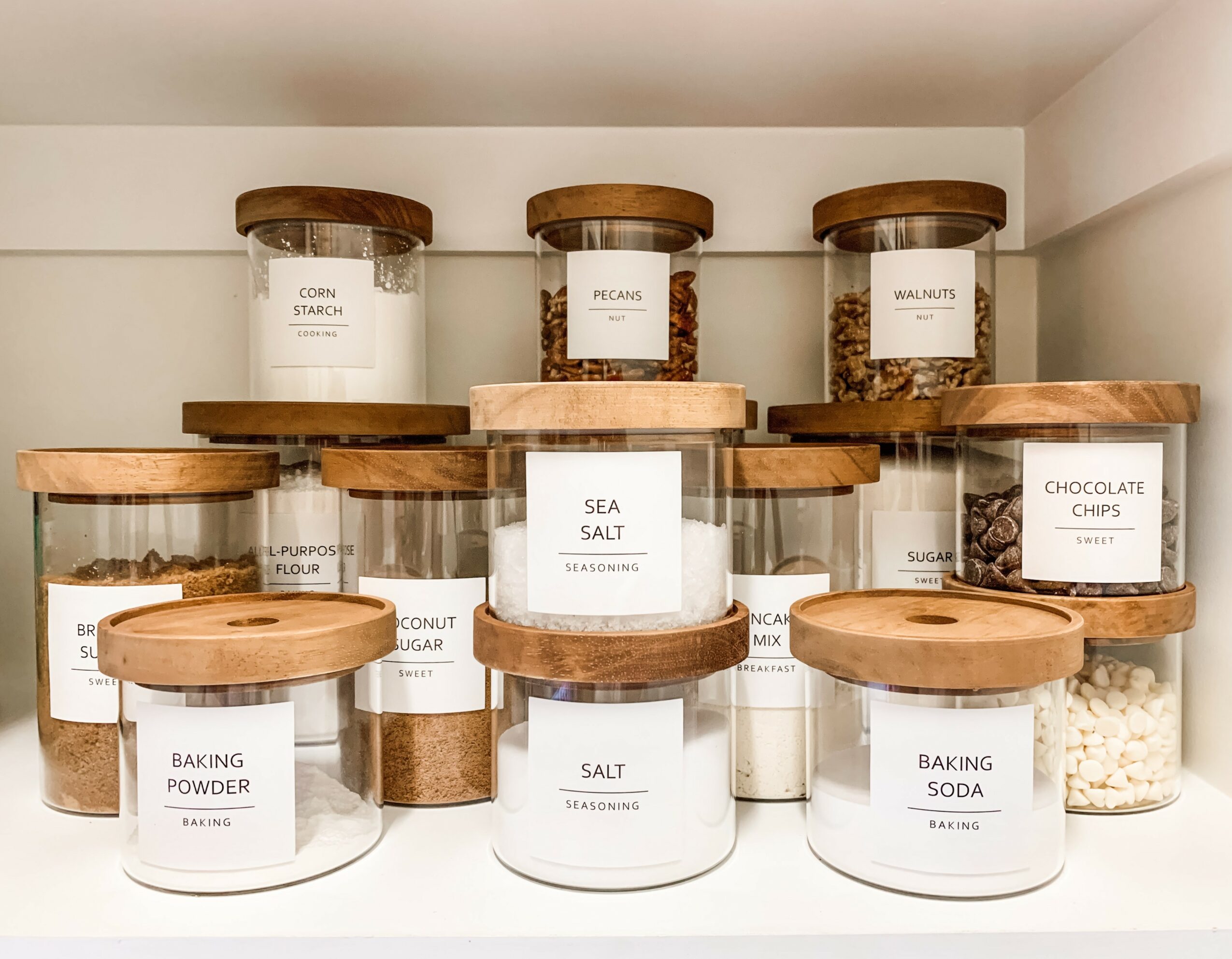 Shelf with glass jars labeled with baking ingredients, including sea salt, chocolate chips, and baking powder.