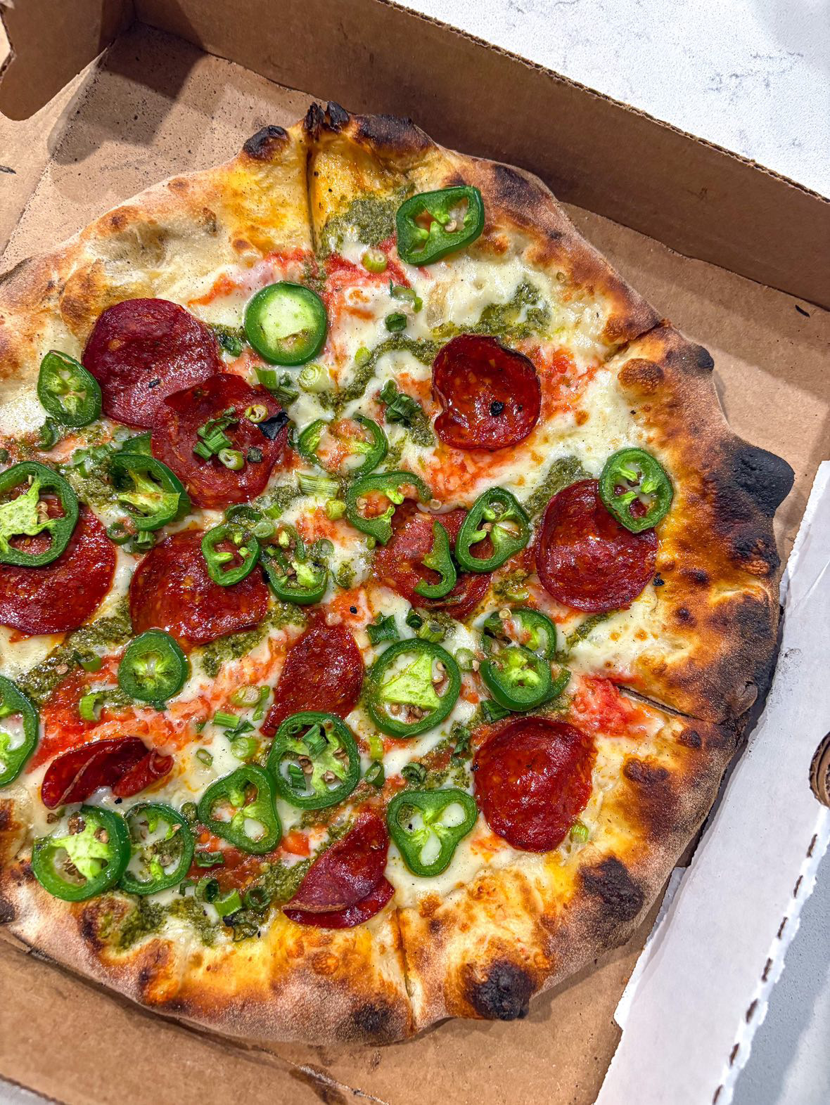 Pizza with pepperoni and sliced green jalapeños in a box, cheese and toppings visible.
