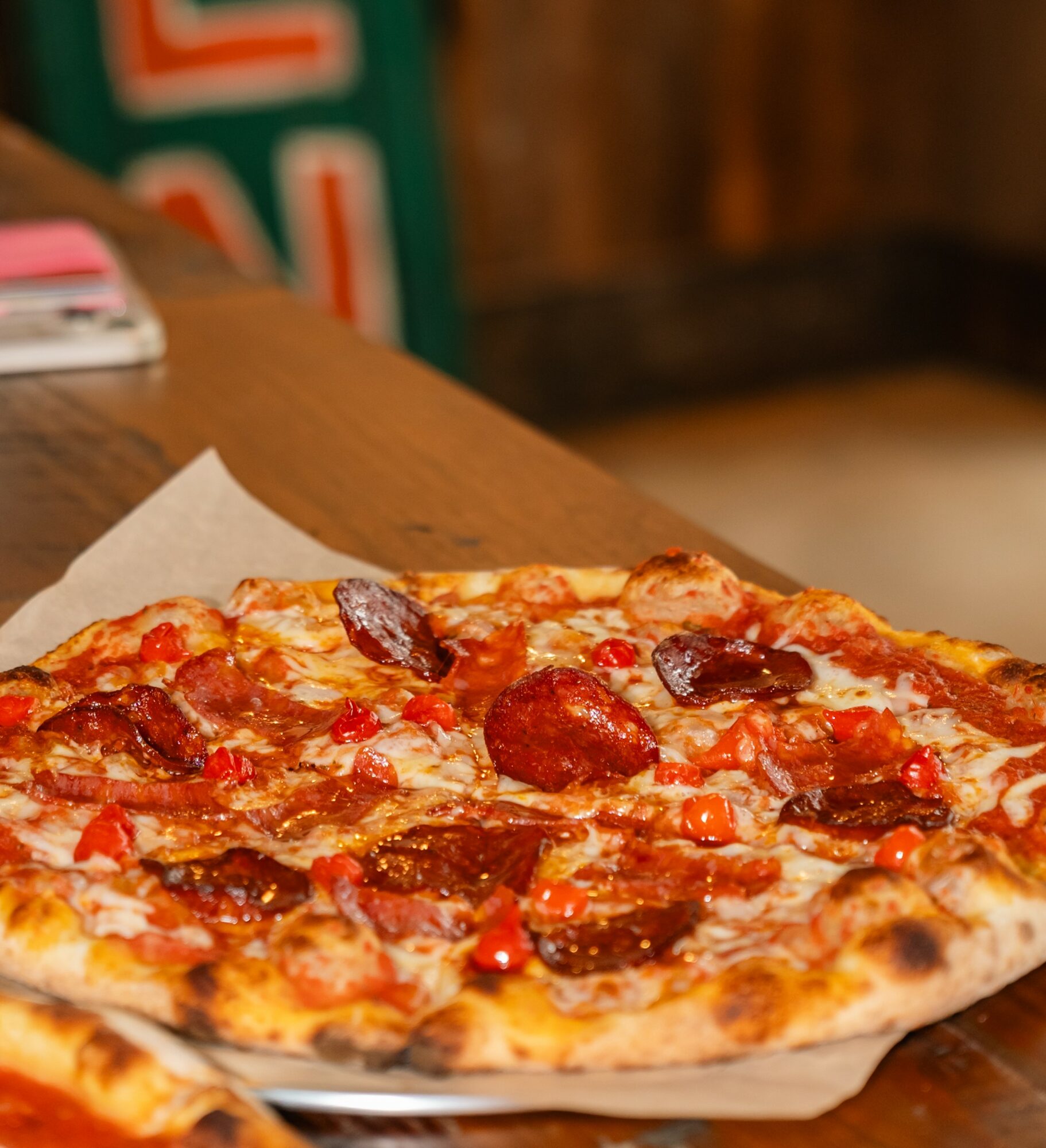 A pizza with pepperoni and sausage on a paper-lined tray, placed on a wooden table in a restaurant setting.