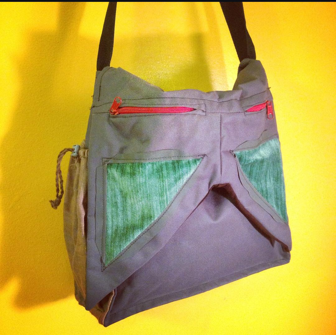 Gray bag with green mesh pockets and red zippers hanging against a yellow background.