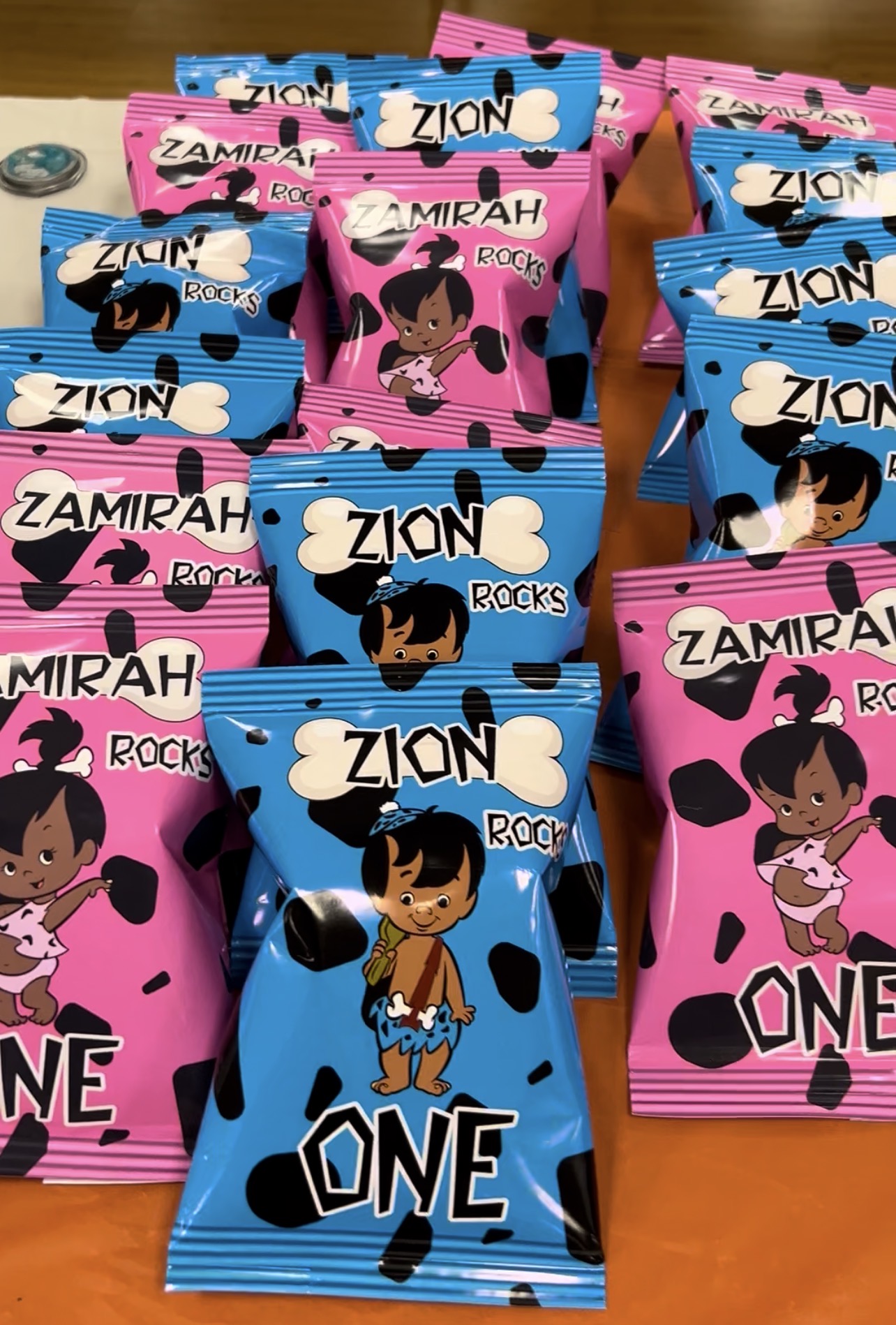 Multiple snack packs with cartoon characters, pink and blue packaging, on a wooden surface.