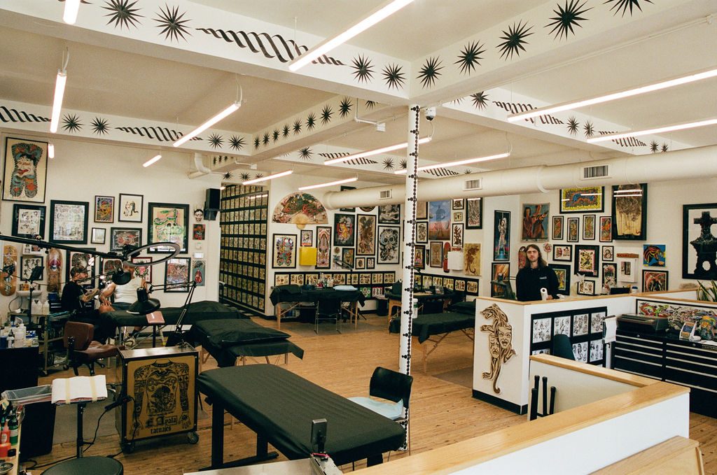 Art gallery with framed artworks on white walls, people viewing art, and display tables in a well-lit room.
