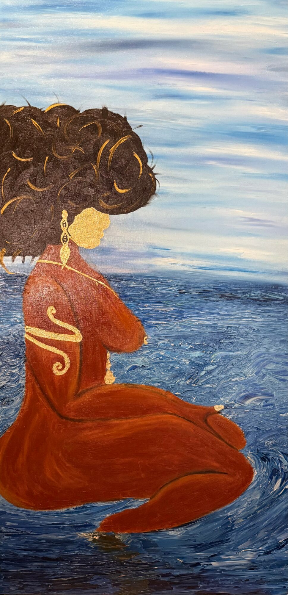 Woman with curly hair sitting by water, wearing a red dress, facing sideways, with a cloudy sky background.