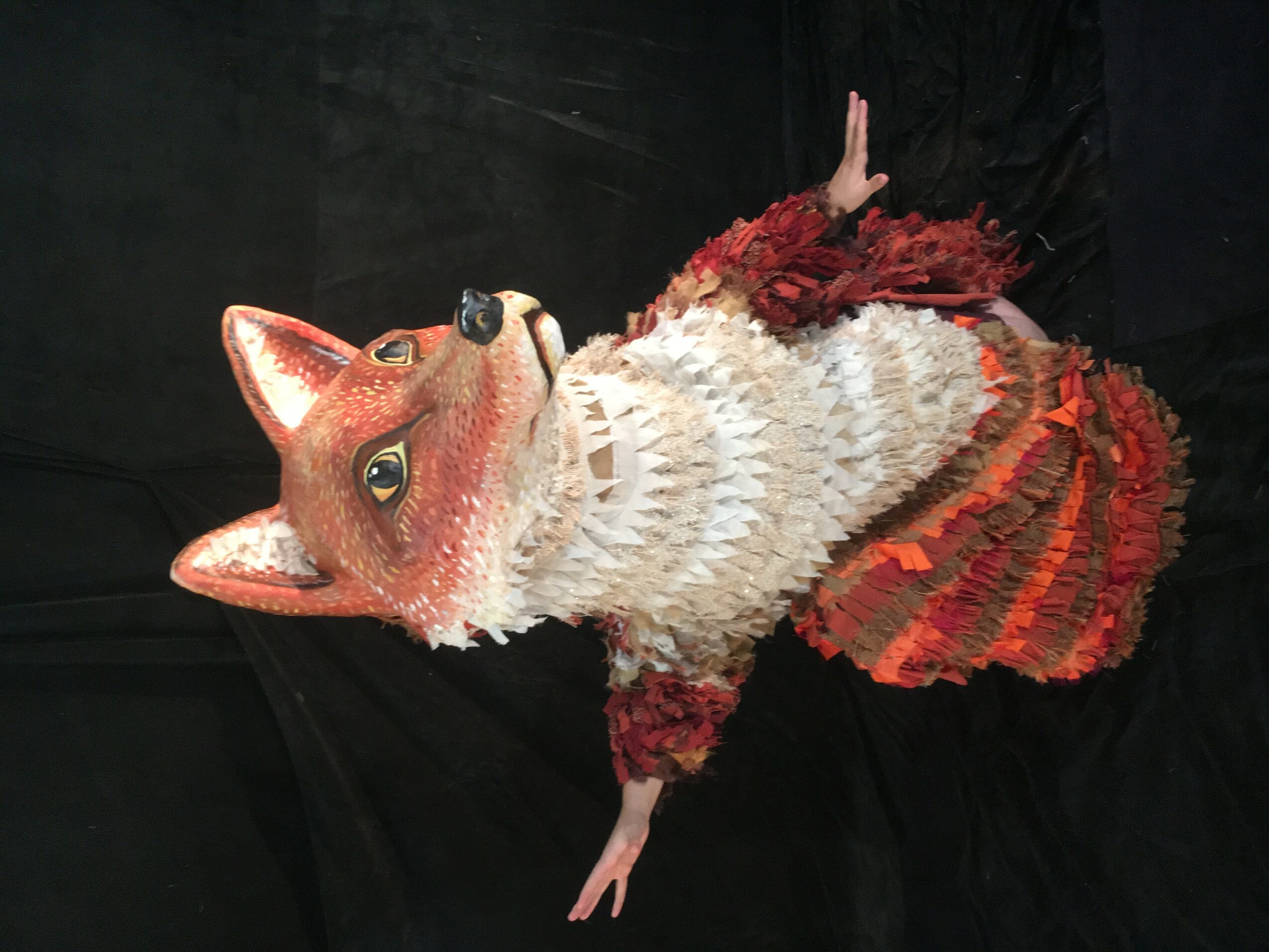 A colorful fox piñata with a detailed face, ears, and a fluffy tail, lying on a black surface.