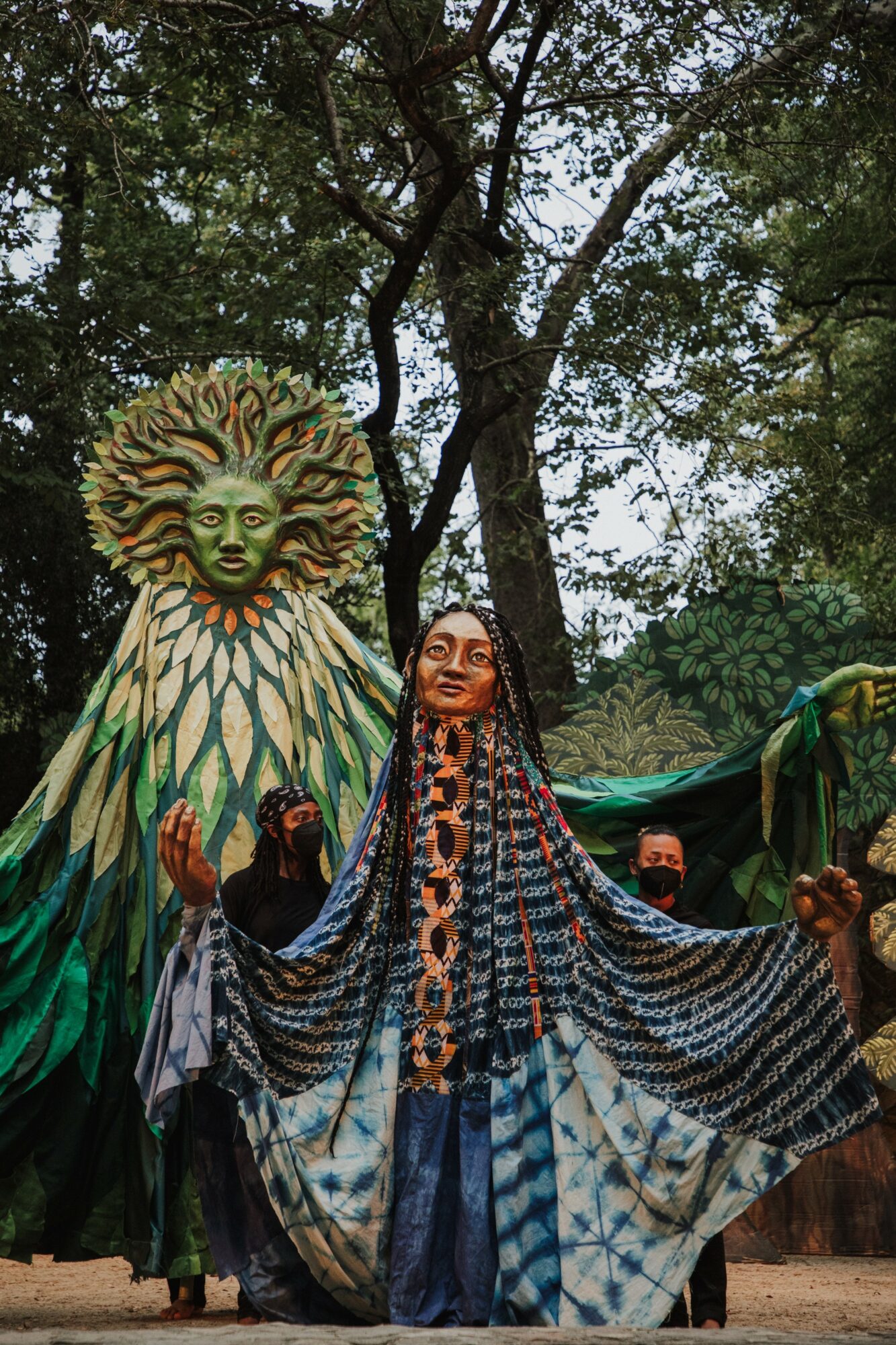 Person with arms outstretched in front of a large lion sculpture outdoors, trees in background.